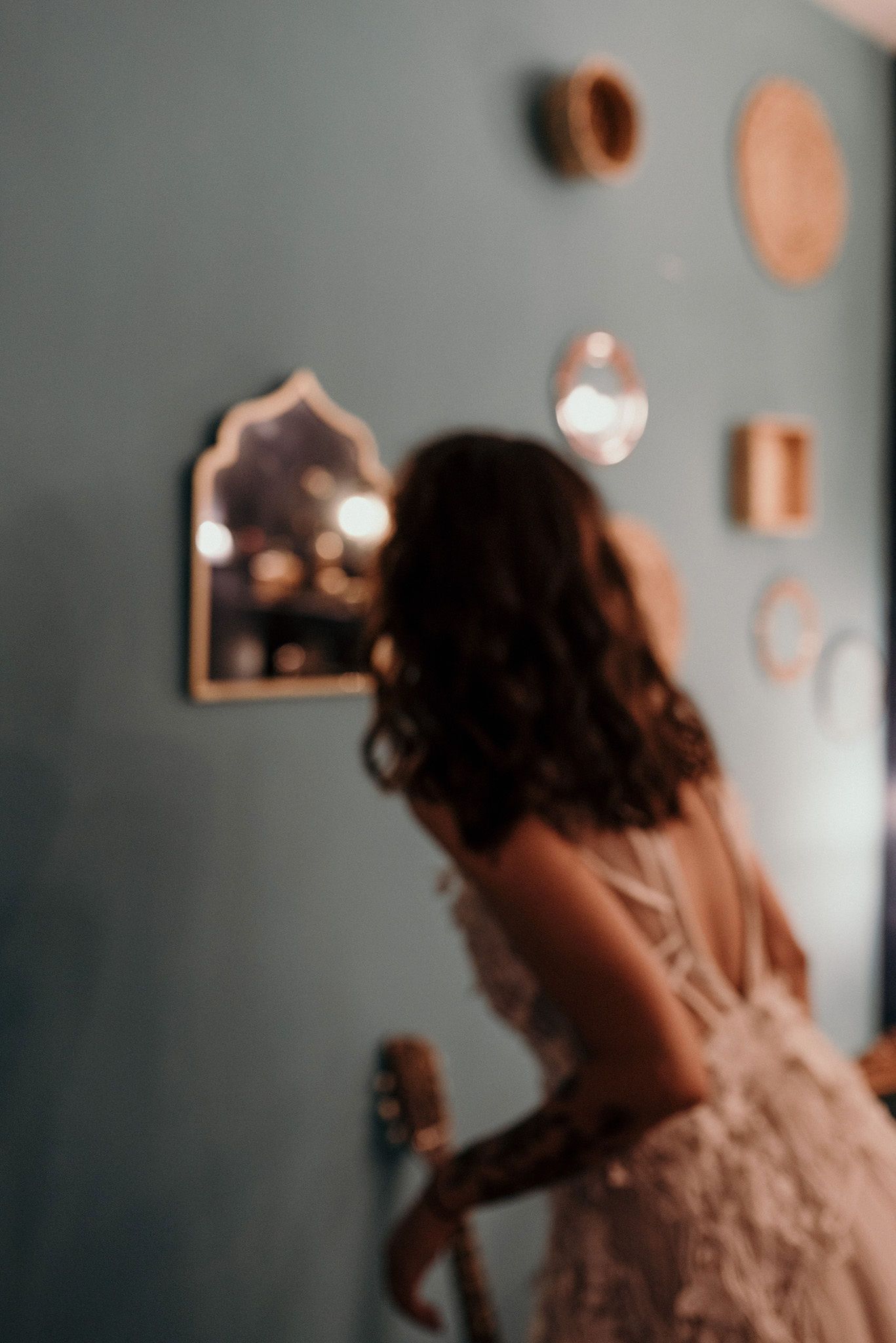 Artistic blurred shot of a wedding dress silhouette against a grey wall with decorative mirrors.