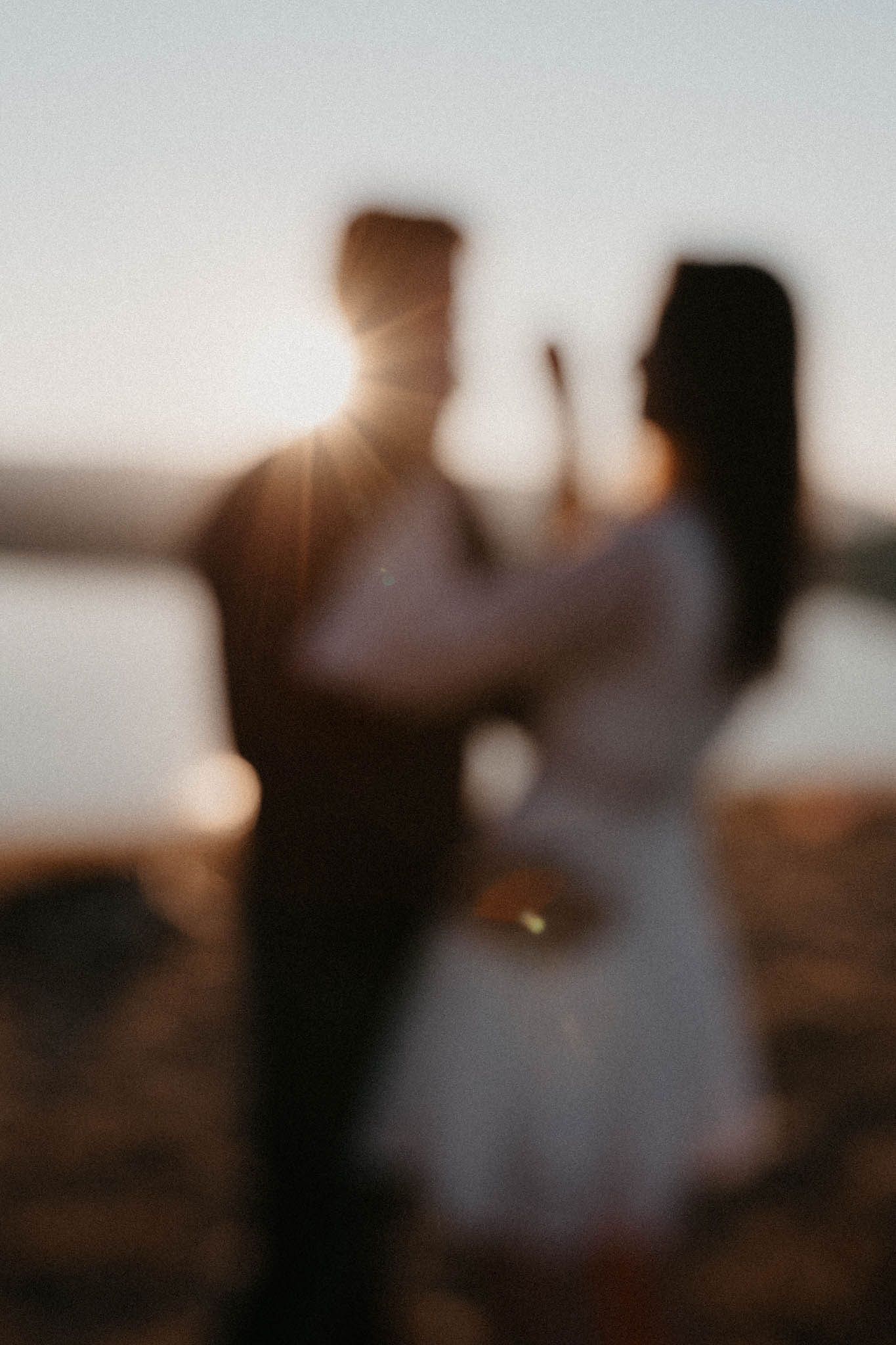Silhouetted figures dancing together against sunset sky over mountain lake.