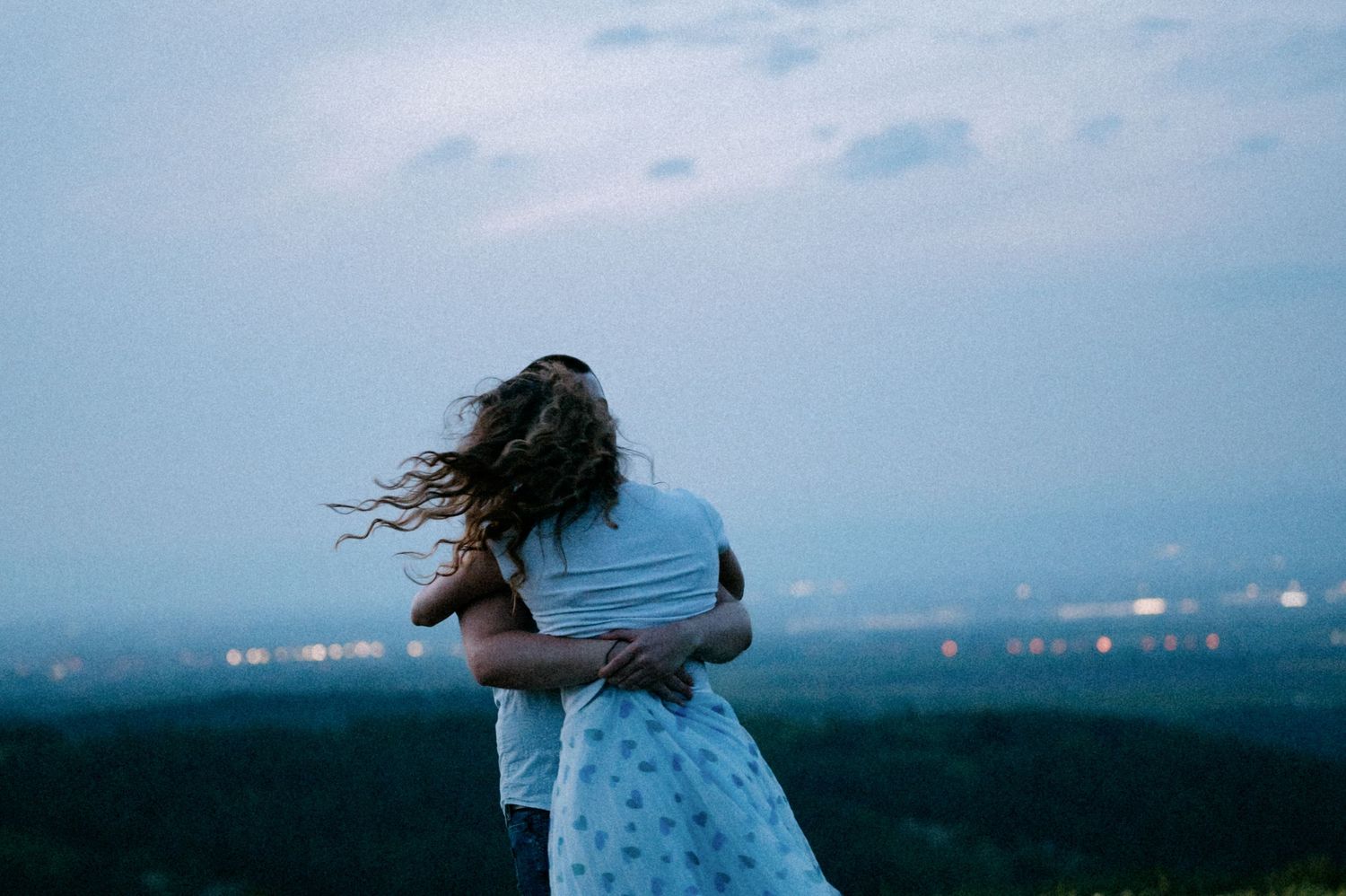 Silhouettes of a dancing couple against a dusky blue sky and distant city lights.