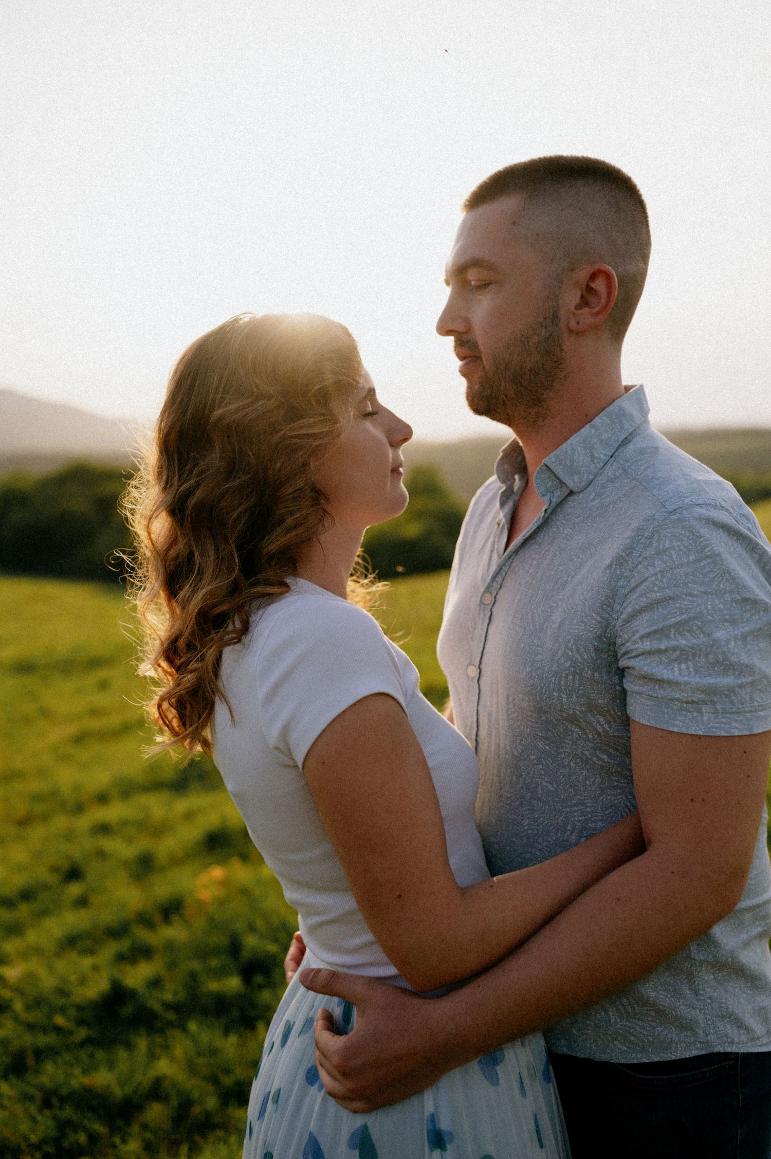 A couple embraces closely while standing in a grassy meadow during golden hour.