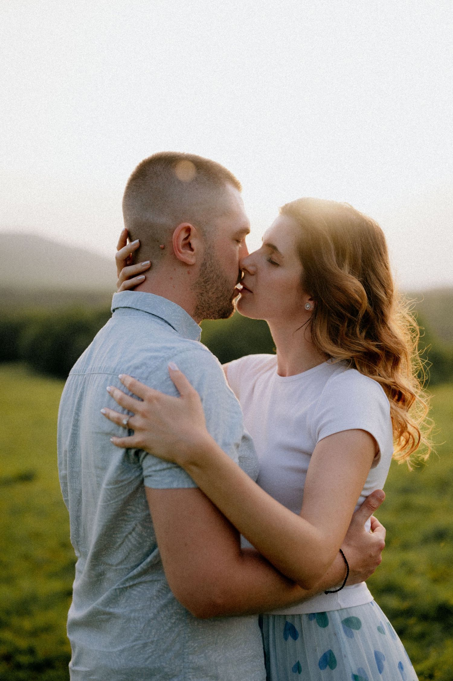 Romantic couple embracing in a grassy field during sunset.