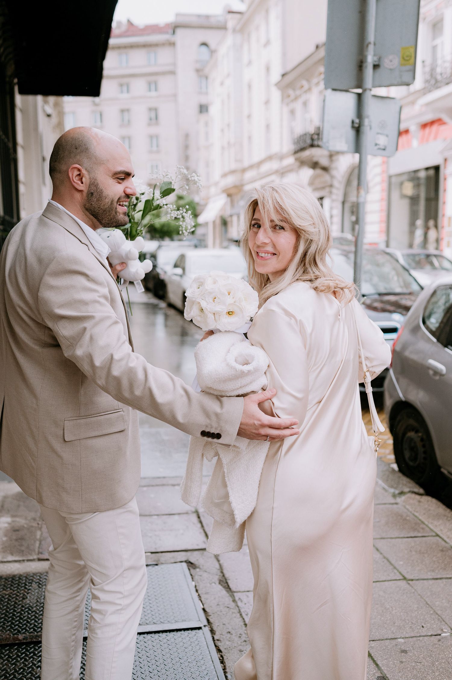 A couple in light colored outfits shares a sweet moment on a city street.