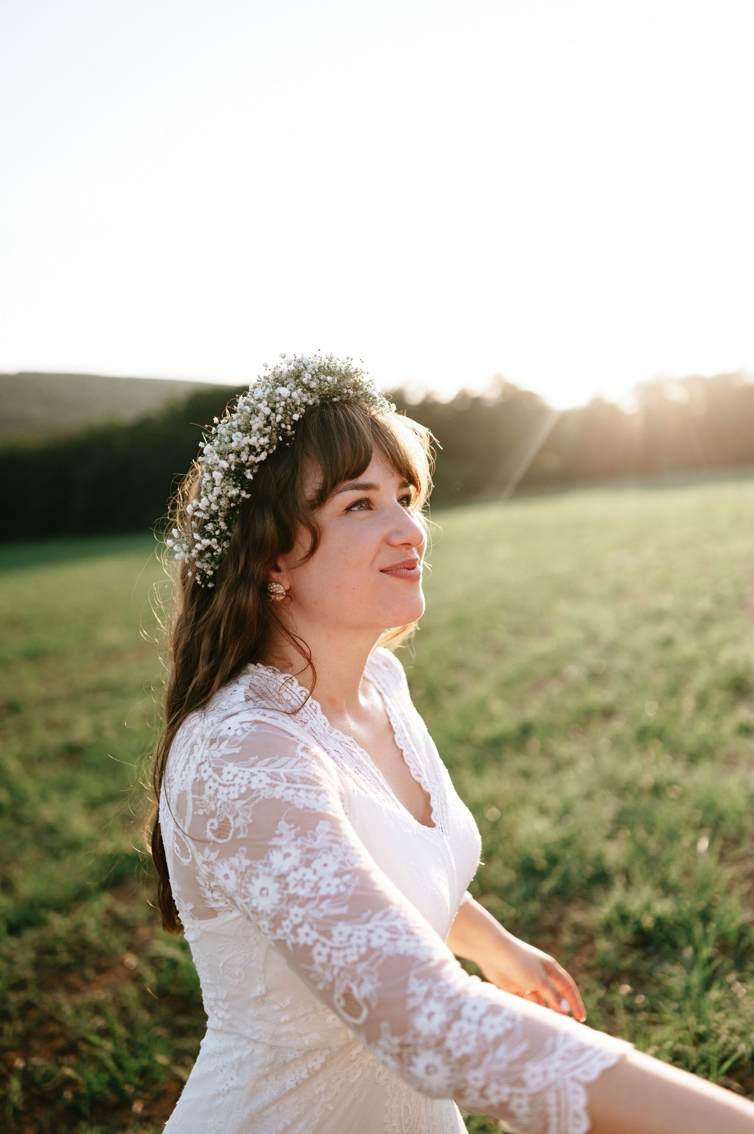 Candid portrait of joyful bride wearing lace dress and flower crown in golden light.