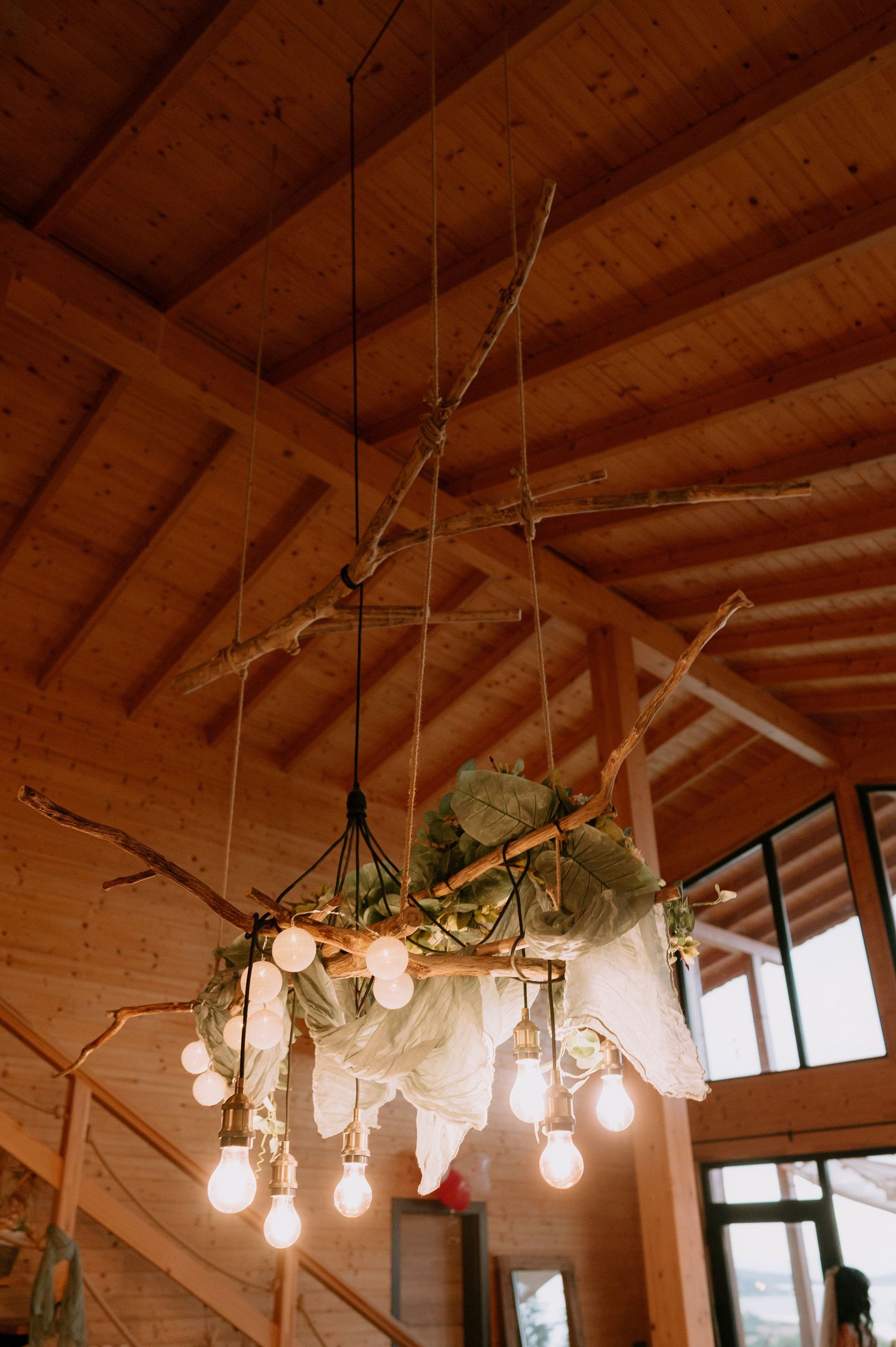 Rustic wooden ceiling with hanging light bulbs and decorative greenery creates warm ambiance.