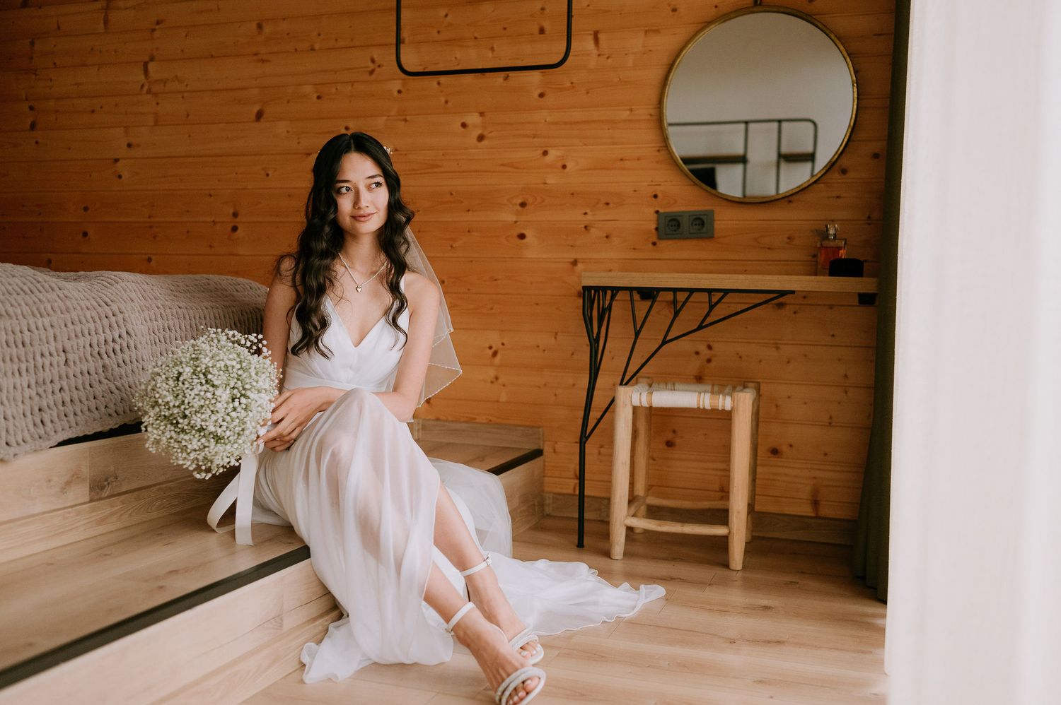 A dreamy bridal portrait featuring a flowing white dress and baby's breath bouquet in a rustic wooden room.