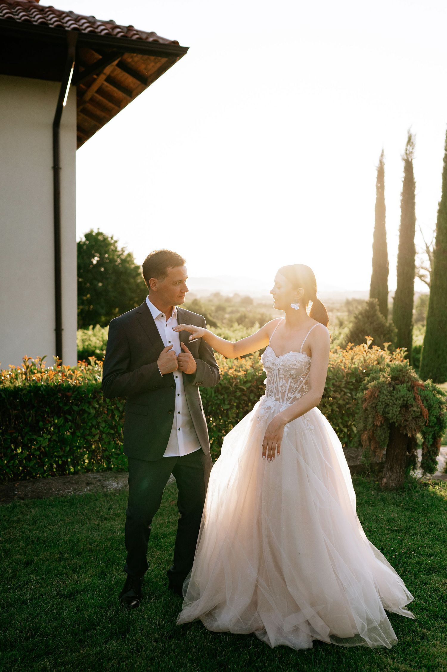 Wedding couple dancing and twirling in a garden with cypress trees at sunset.