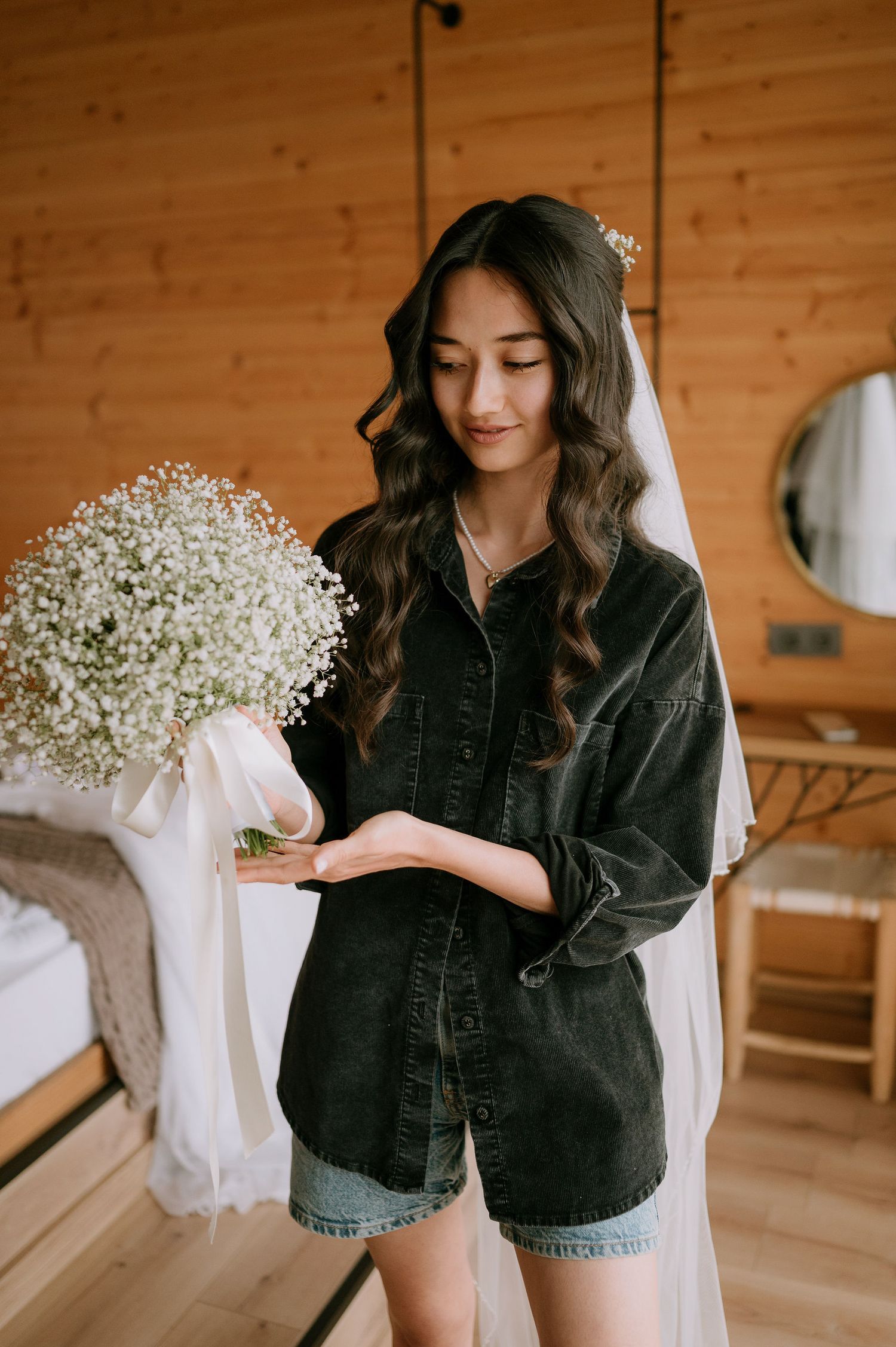 Woman in denim holding white floral arrangement in sunlit wooden interior.