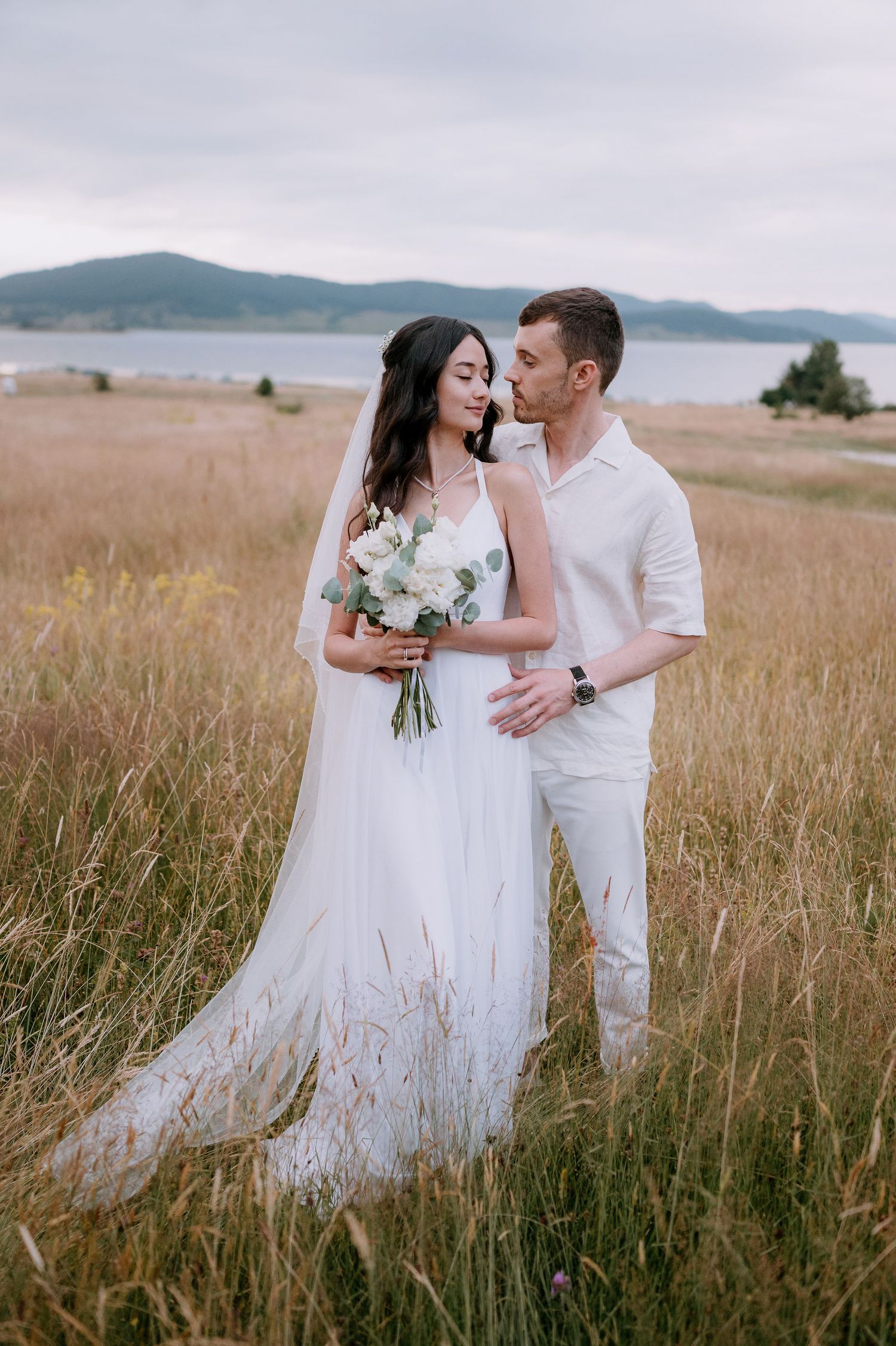 Elegant wedding couple poses together in golden grass with scenic mountain views.