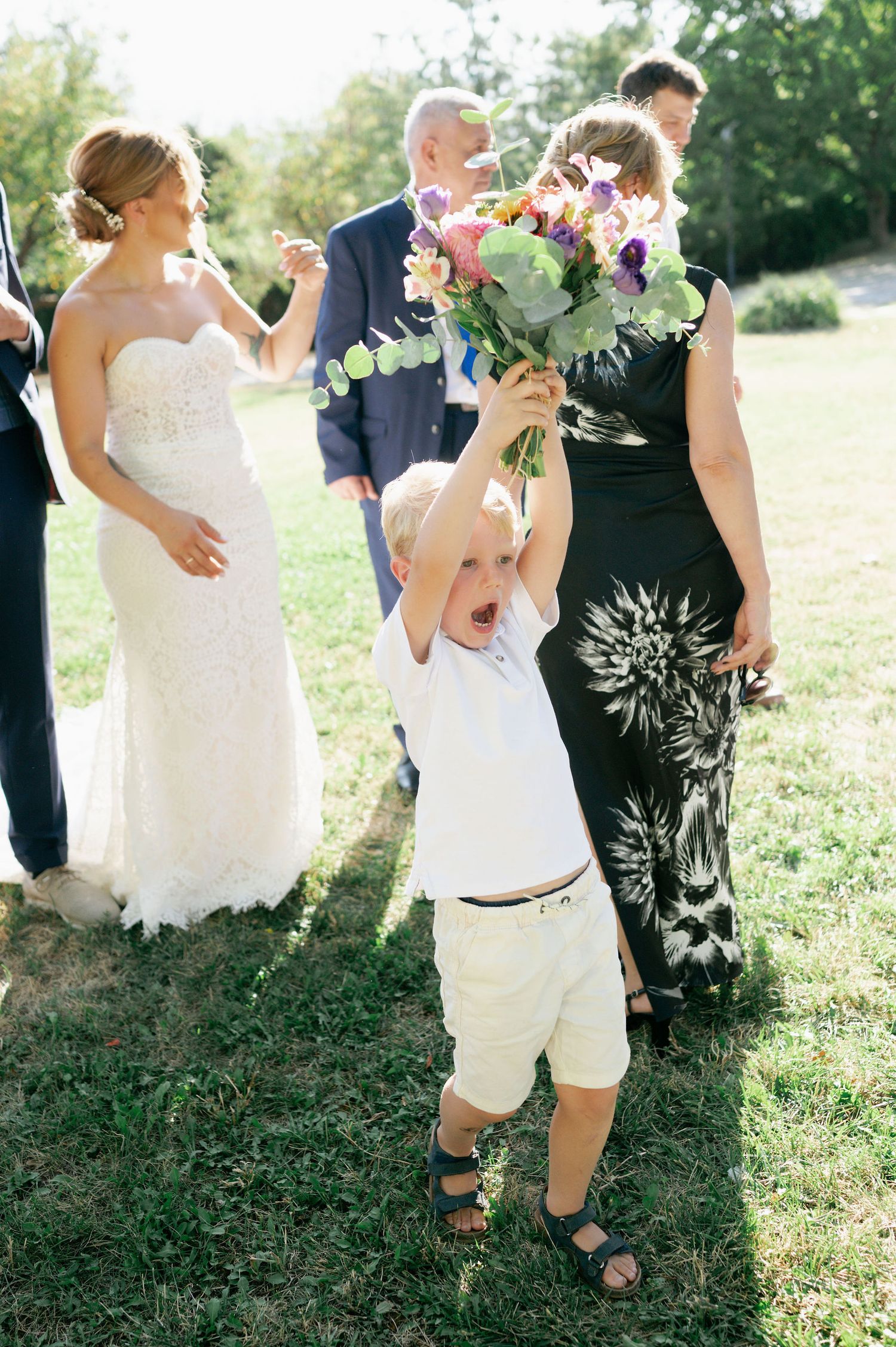 Wedding party members dance and celebrate on a sunlit lawn during an outdoor reception.