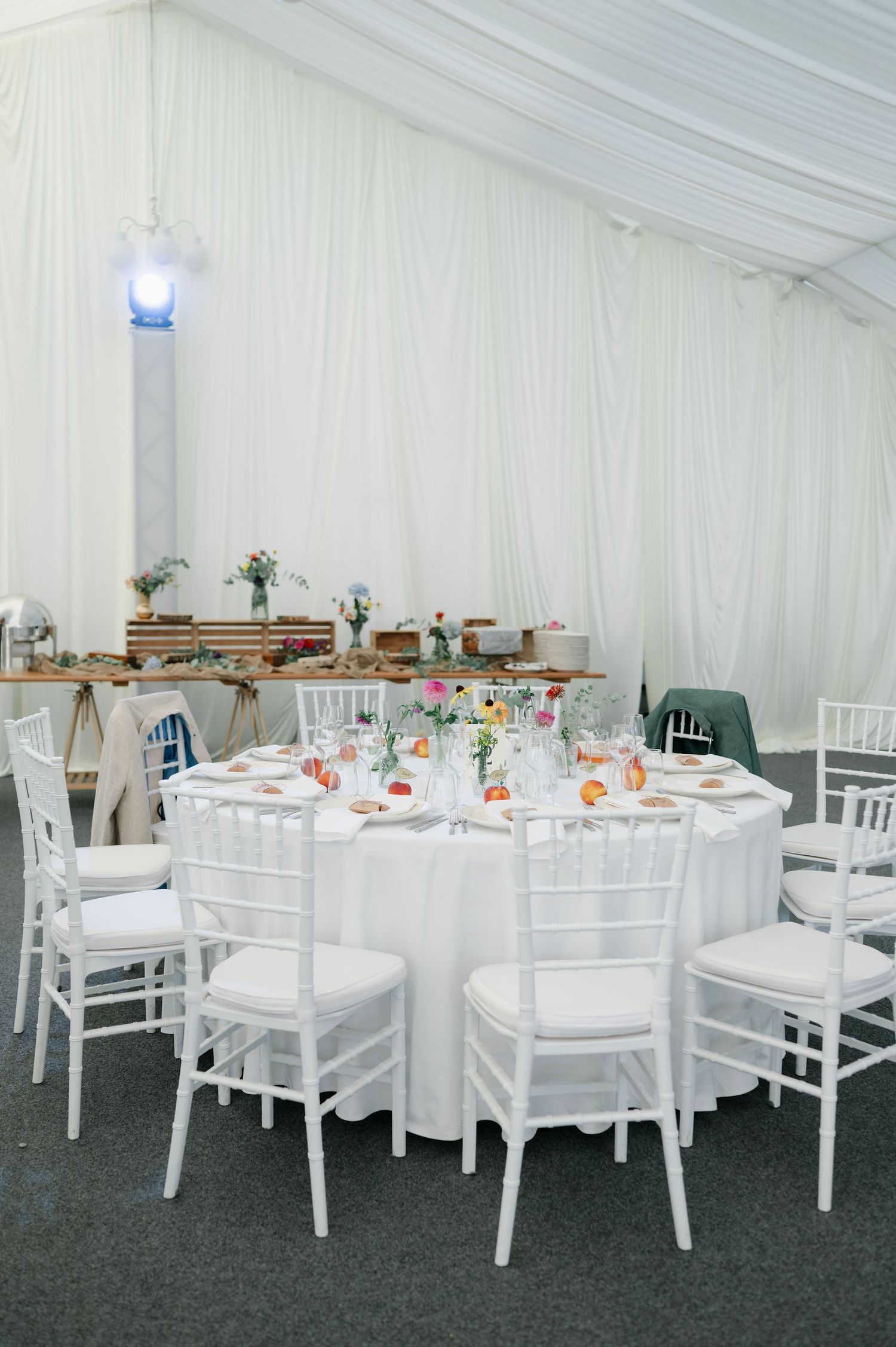 White wedding reception tables arranged in a tent with floral centerpieces and place settings.