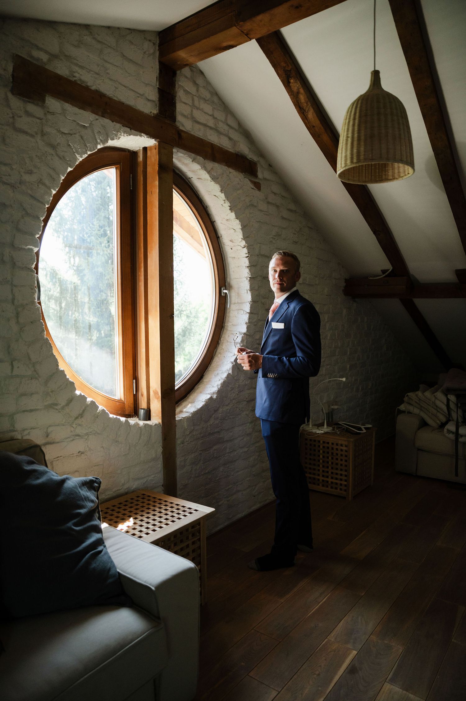 A bright attic space with exposed beams features a round window and white painted brick walls.