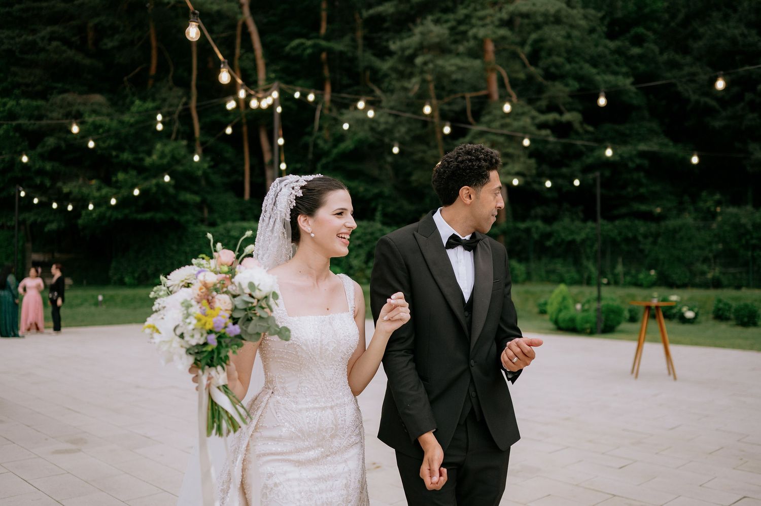 A romantic wedding moment captured under string lights in an outdoor garden setting.