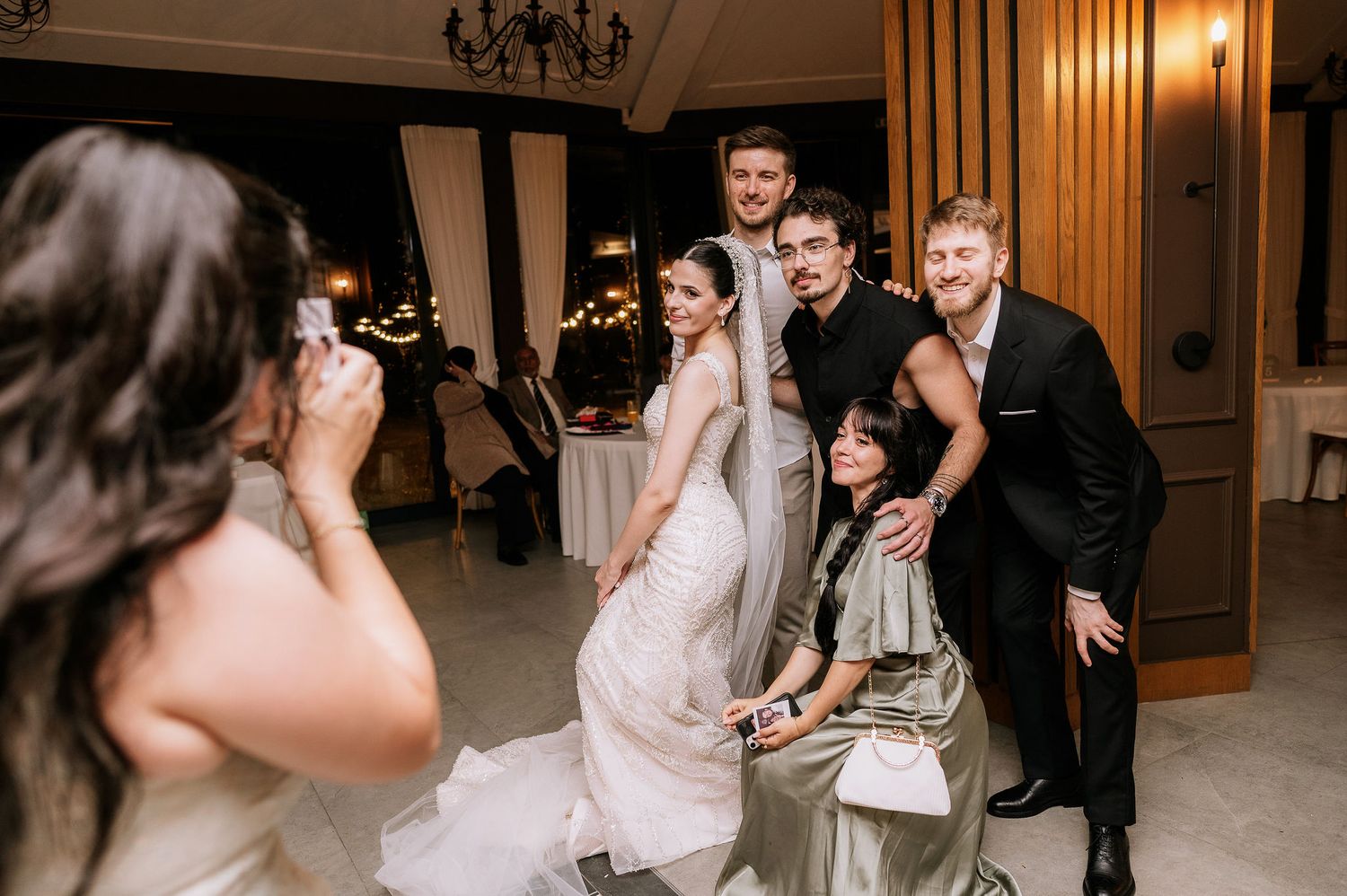 Wedding party poses together for photos in an elegant indoor venue with chandeliers.