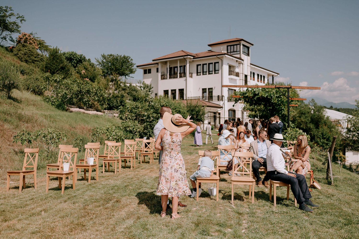 A panoramic view of an outdoor wedding venue with wooden chairs set up on a grassy hillside.