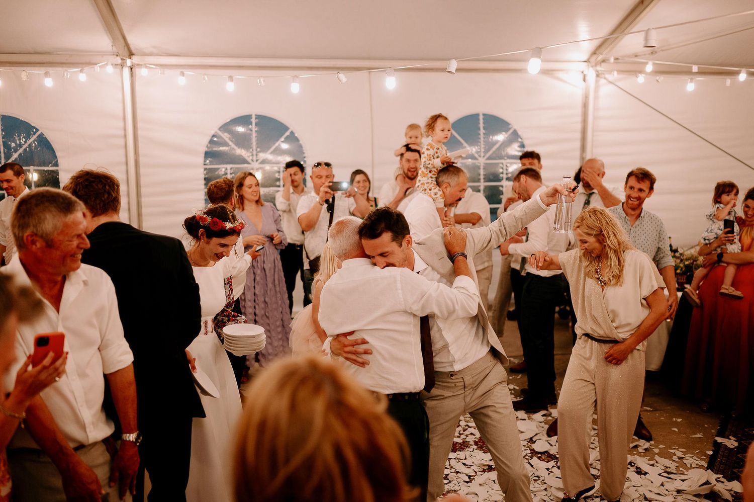 Festive reception scene with guests mingling under string lights in a white tent venue.