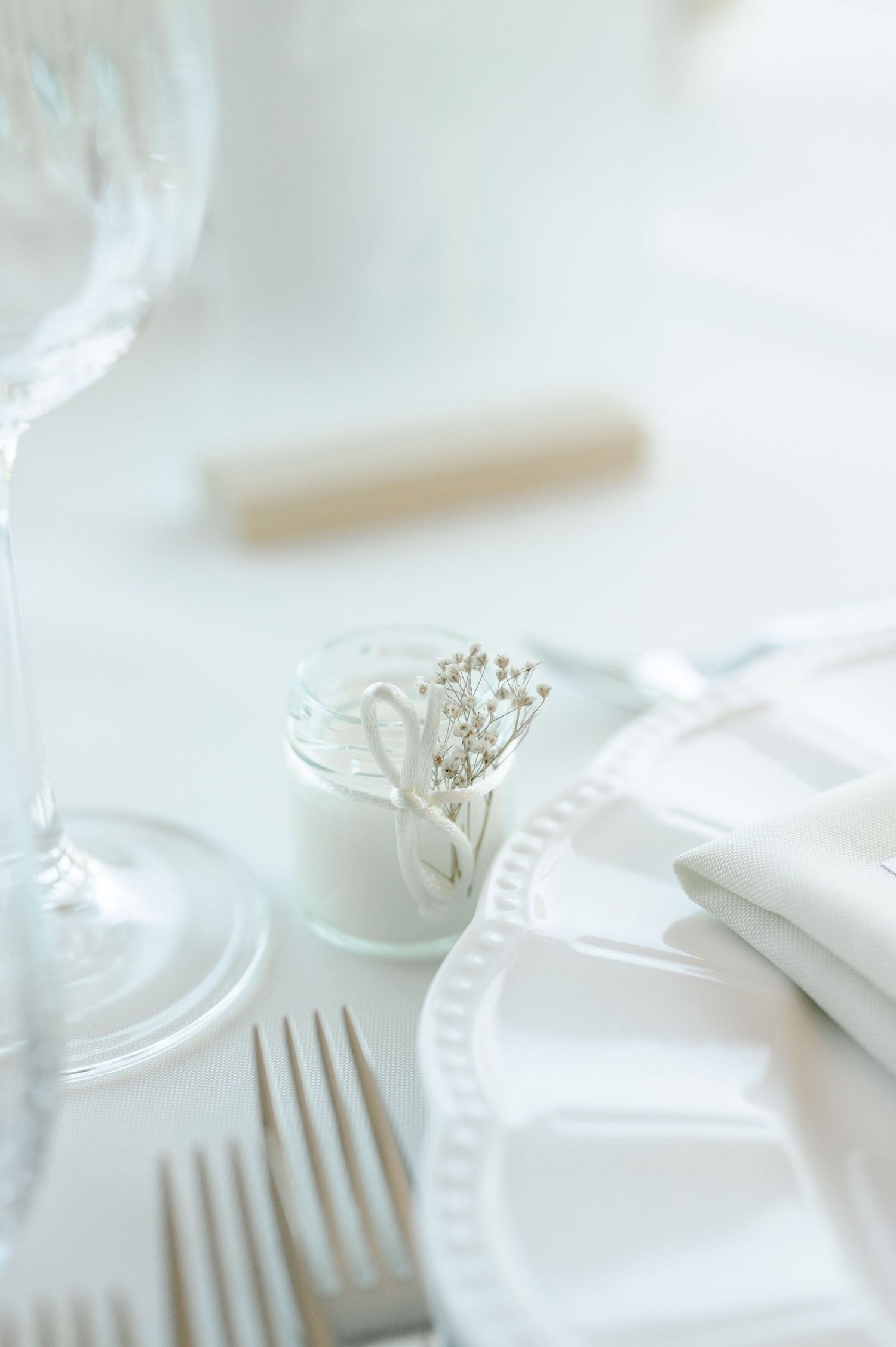 Delicate white place settings with ornate plates and silver cutlery in soft focus.