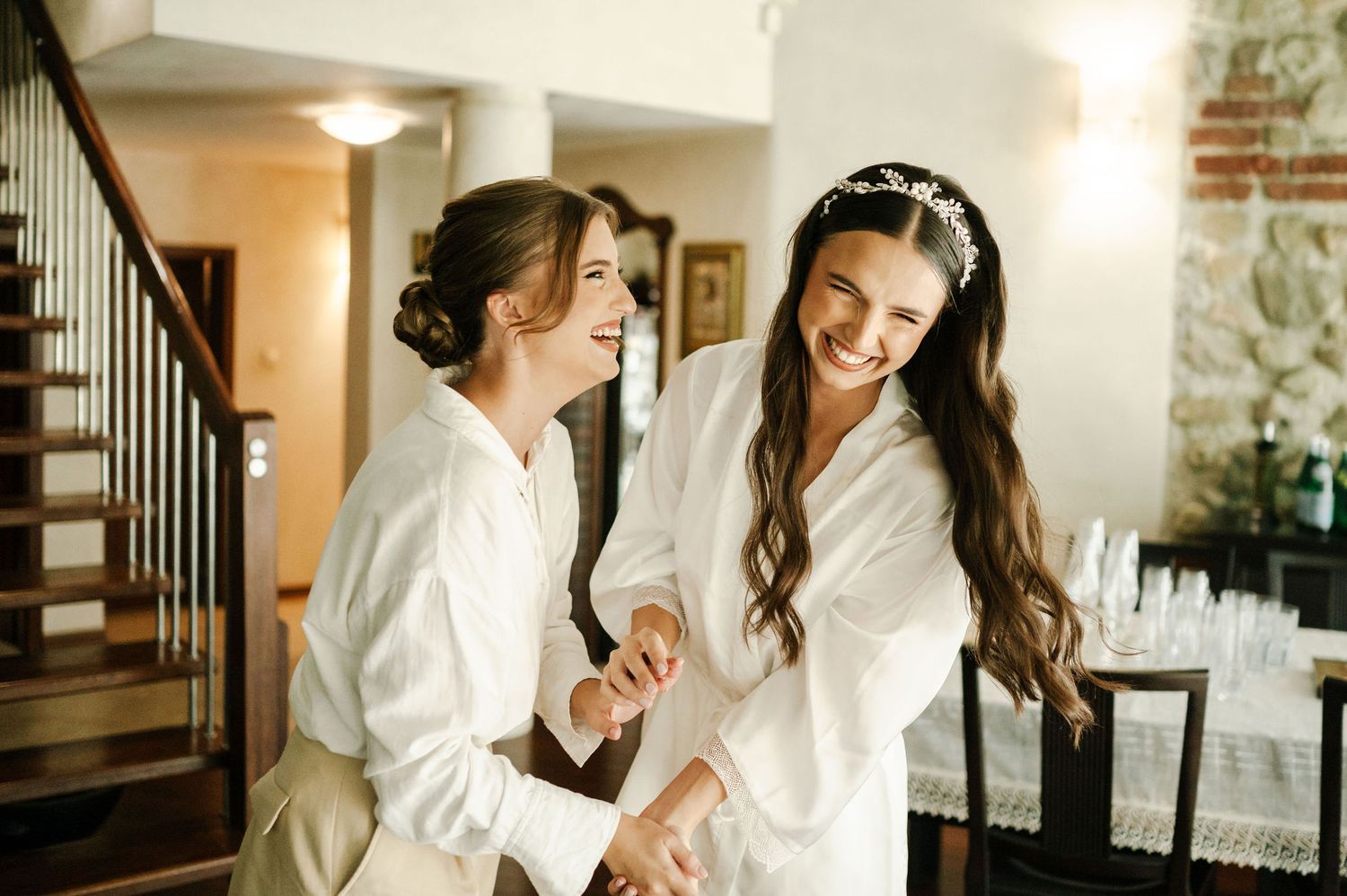 Two women in white robes share an intimate moment while getting ready.