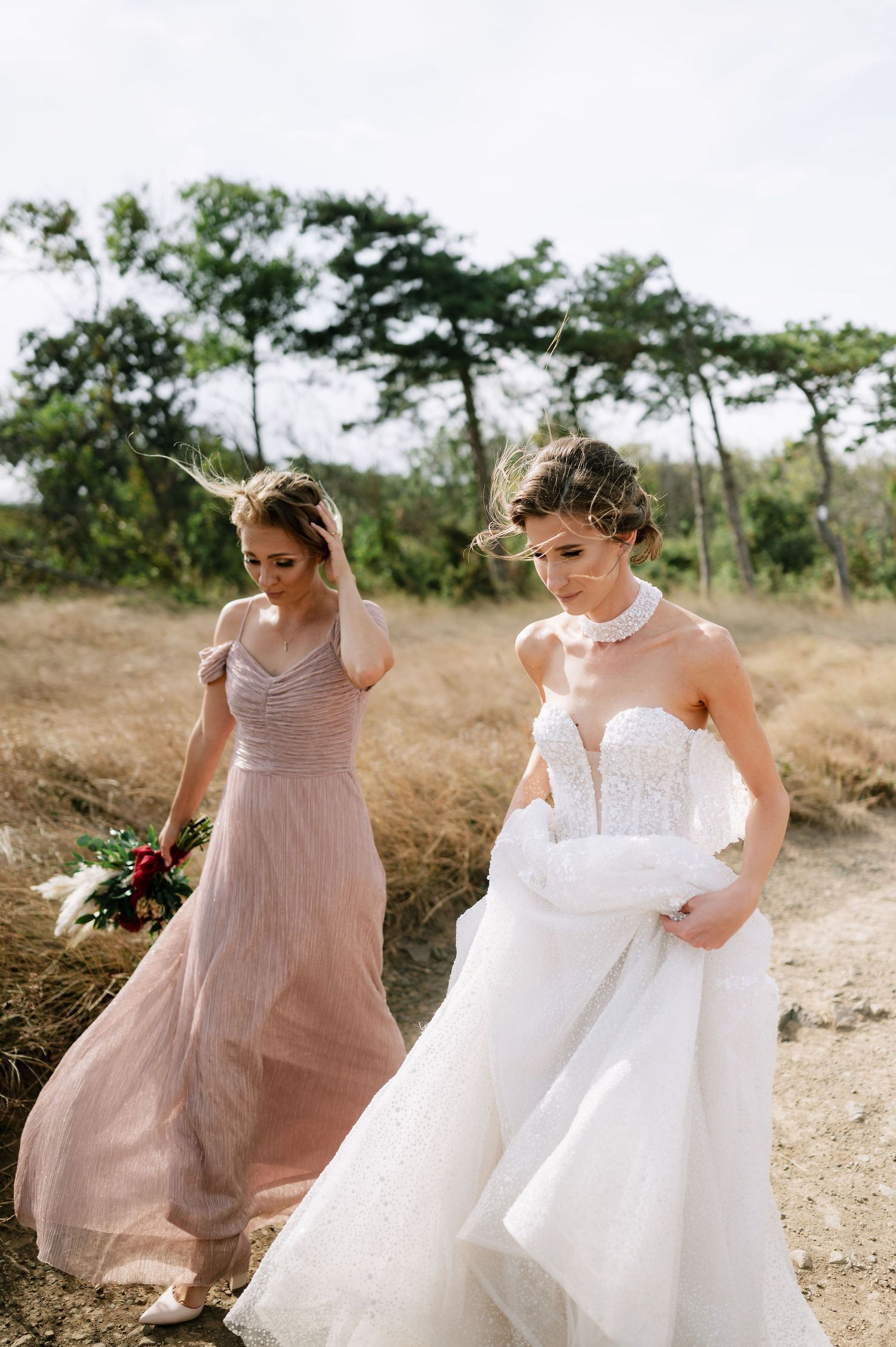 Two people in formal attire walking together on a dirt path surrounded by tall grass.