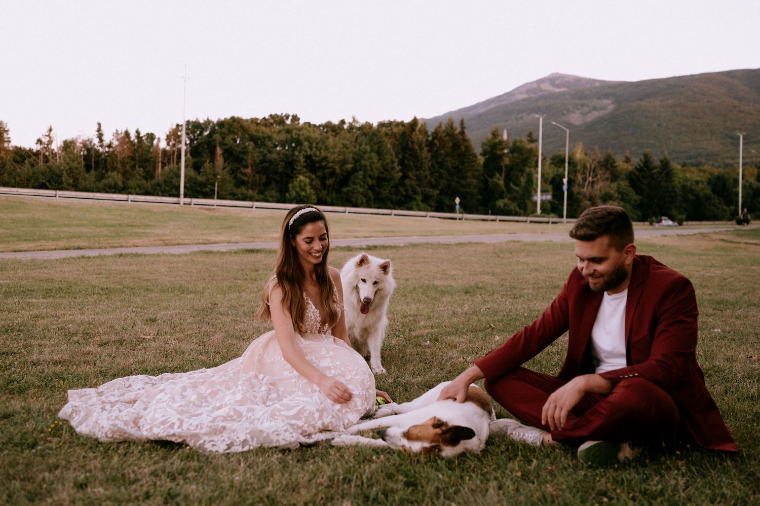 A couple and their white dog relax on grassy hillside during a romantic photoshoot.