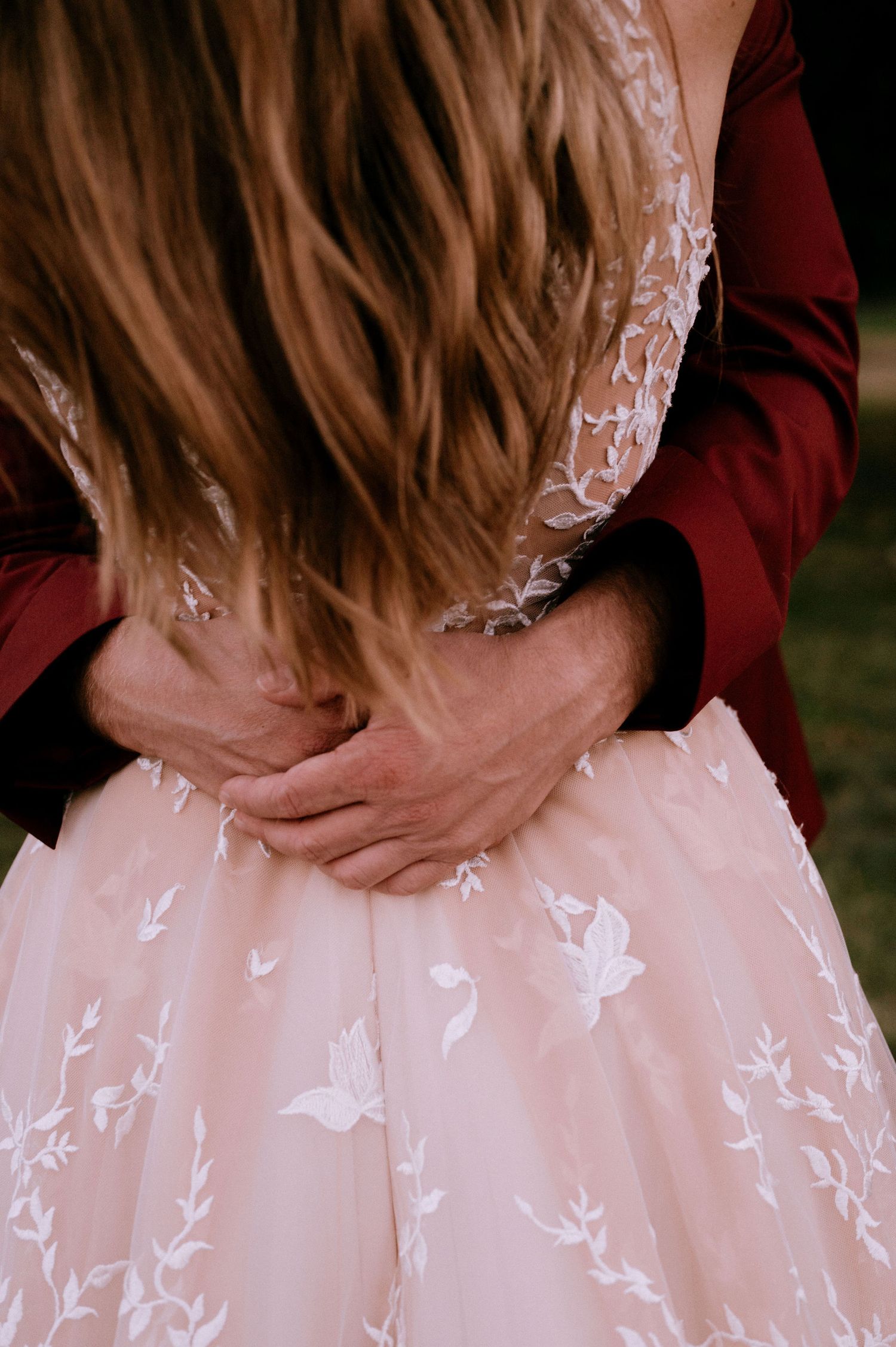 Close-up detail of a blush pink wedding dress with delicate white lace butterflies and floral appliques.