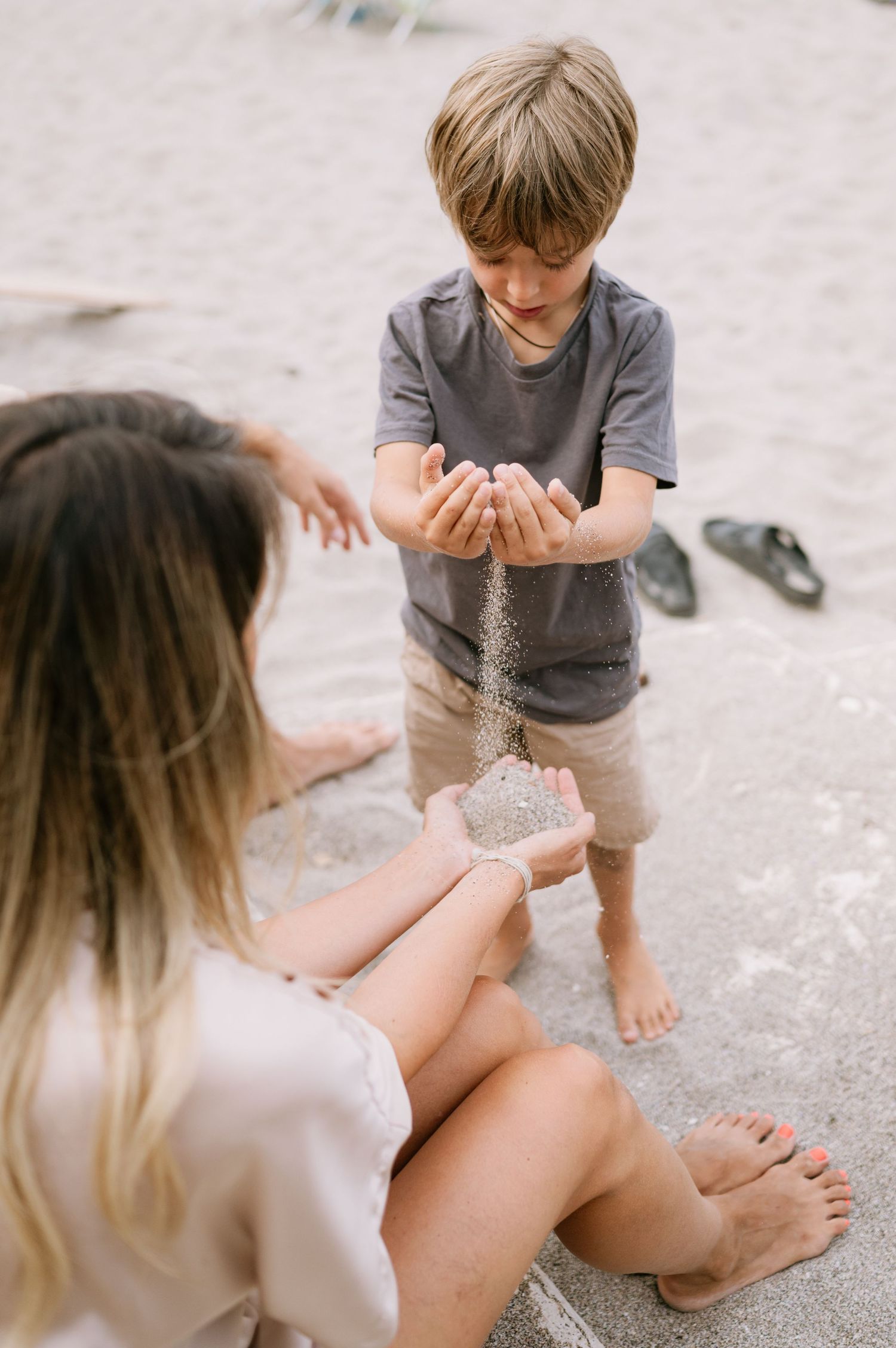 A boy pours sand into a girl's hands on a beach, both barefoot and enjoying a playful moment together.