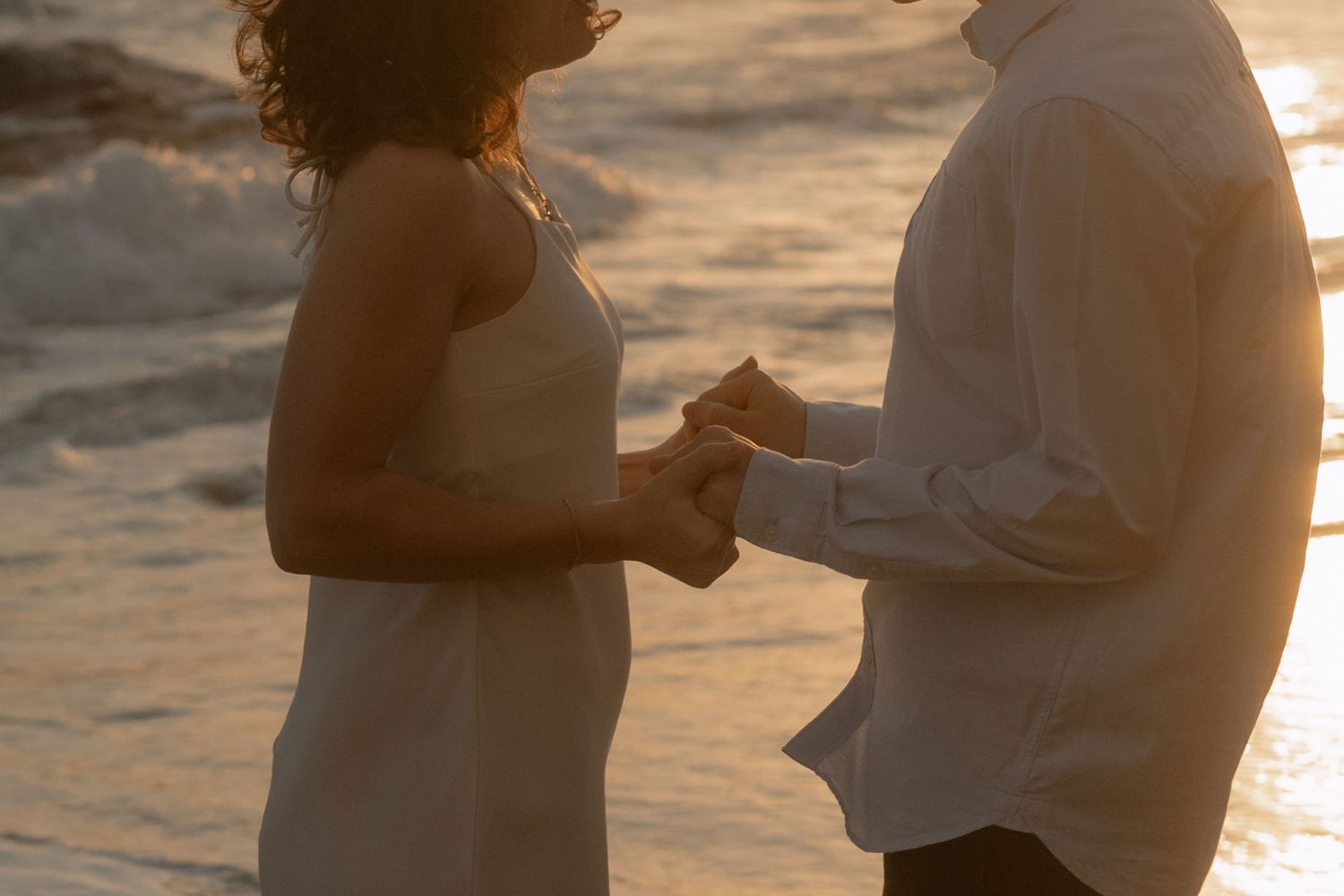 Couple holding hands on a beach at golden sunset, romantic seaside moment.
