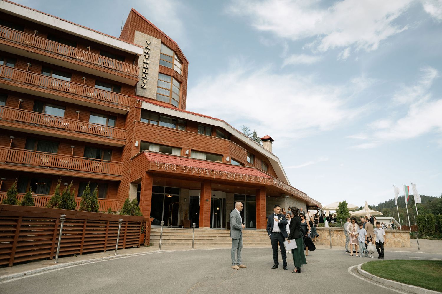 People gather outside a modern red brick building with large windows and steps leading to the entrance.