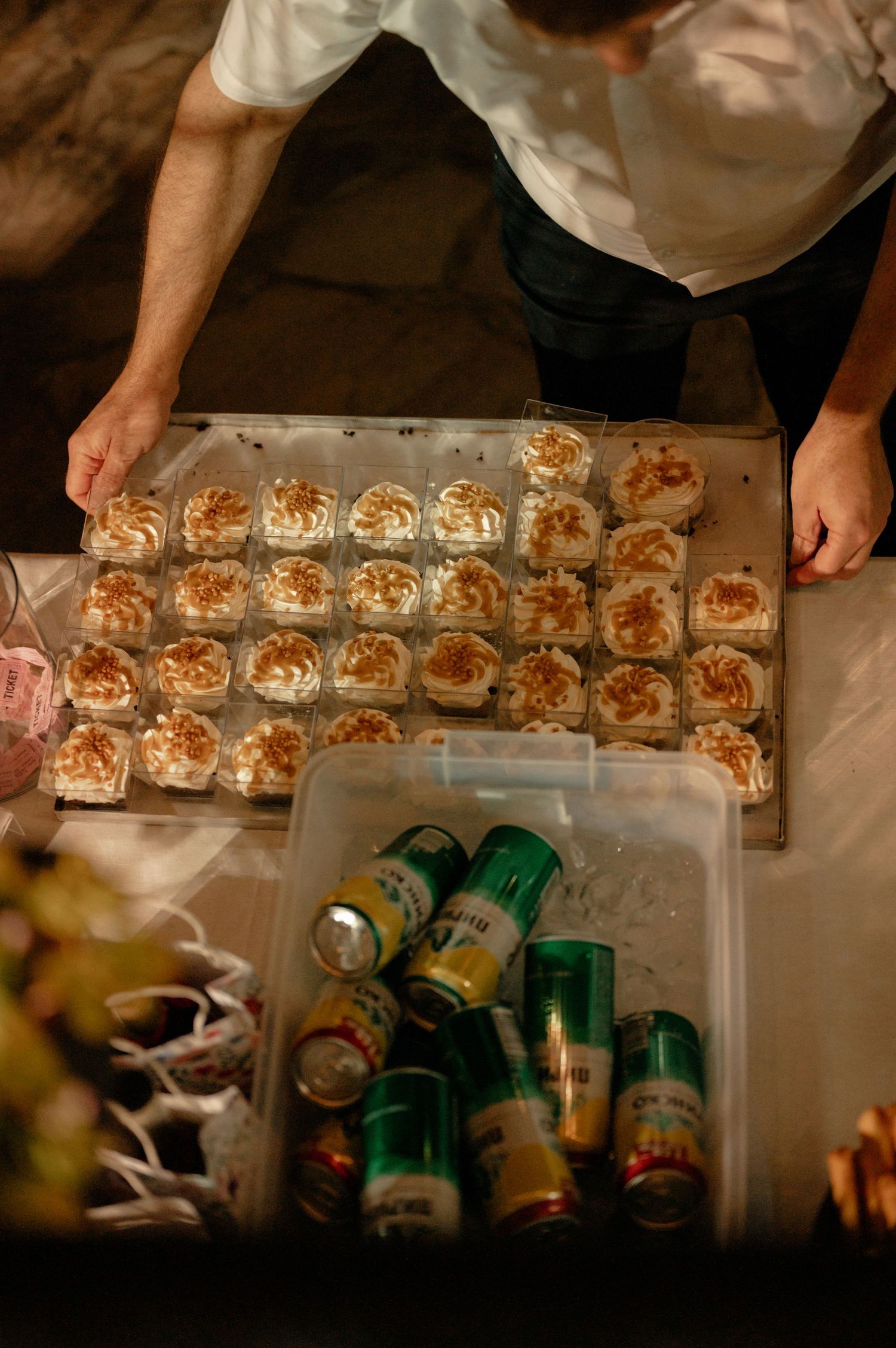 Multiple small appetizer portions are being plated and arranged on a dark surface with green beverage containers visible.