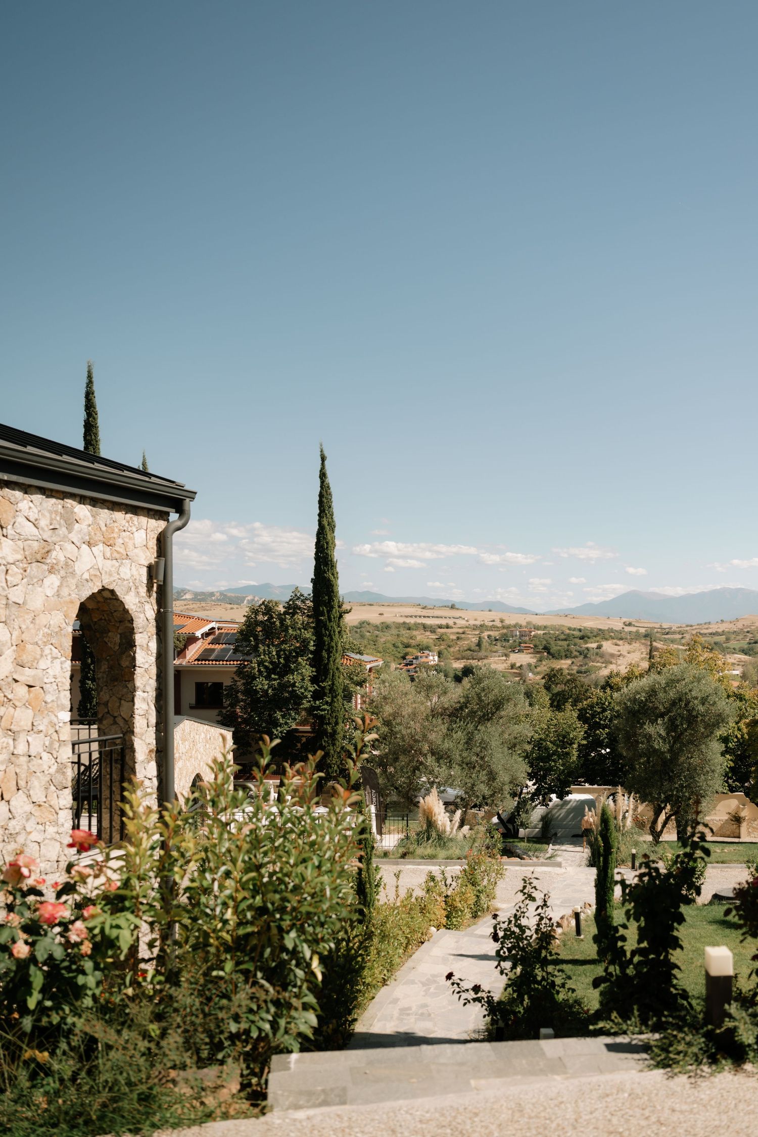 A scenic Tuscan landscape with cypress trees and stone architecture overlooking rolling hills on a sunny day.