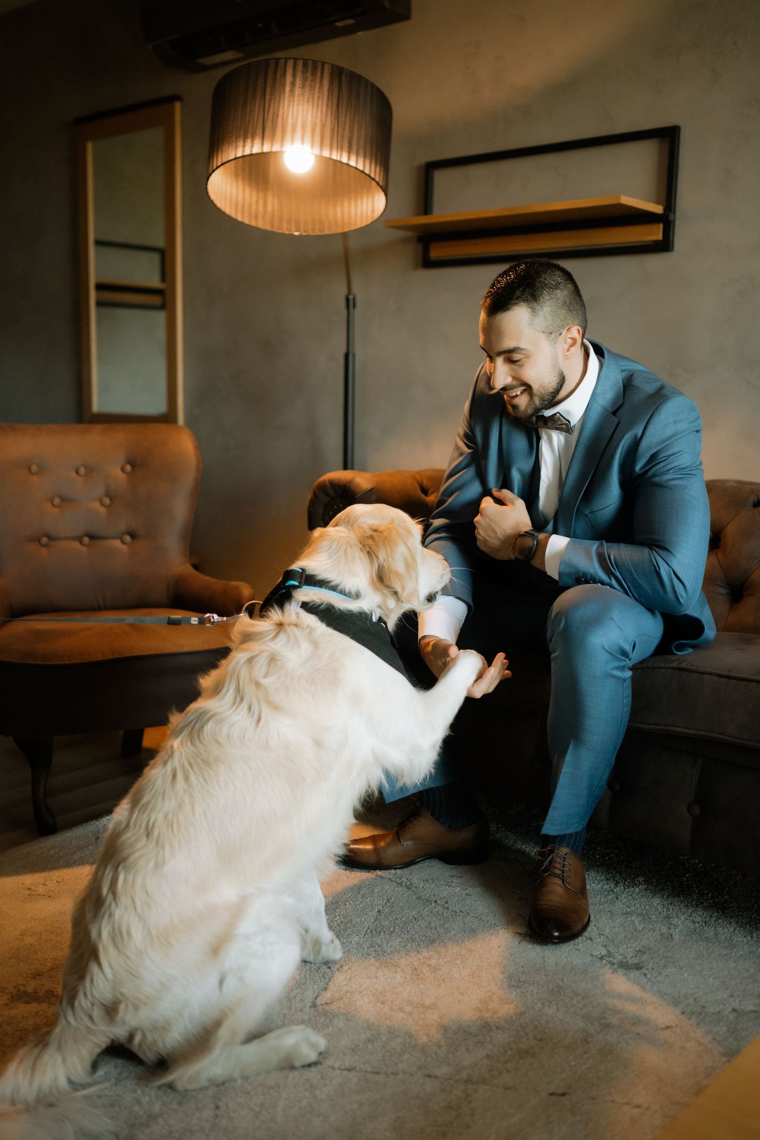 A person in a blue suit plays with a fluffy white dog on a carpeted floor in a dimly lit room.