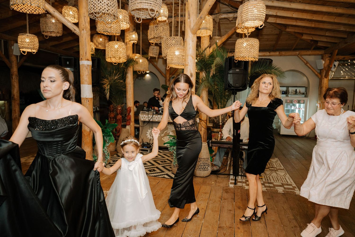 A group of people dancing together at a rustic venue decorated with hanging wicker lamps during a celebration.