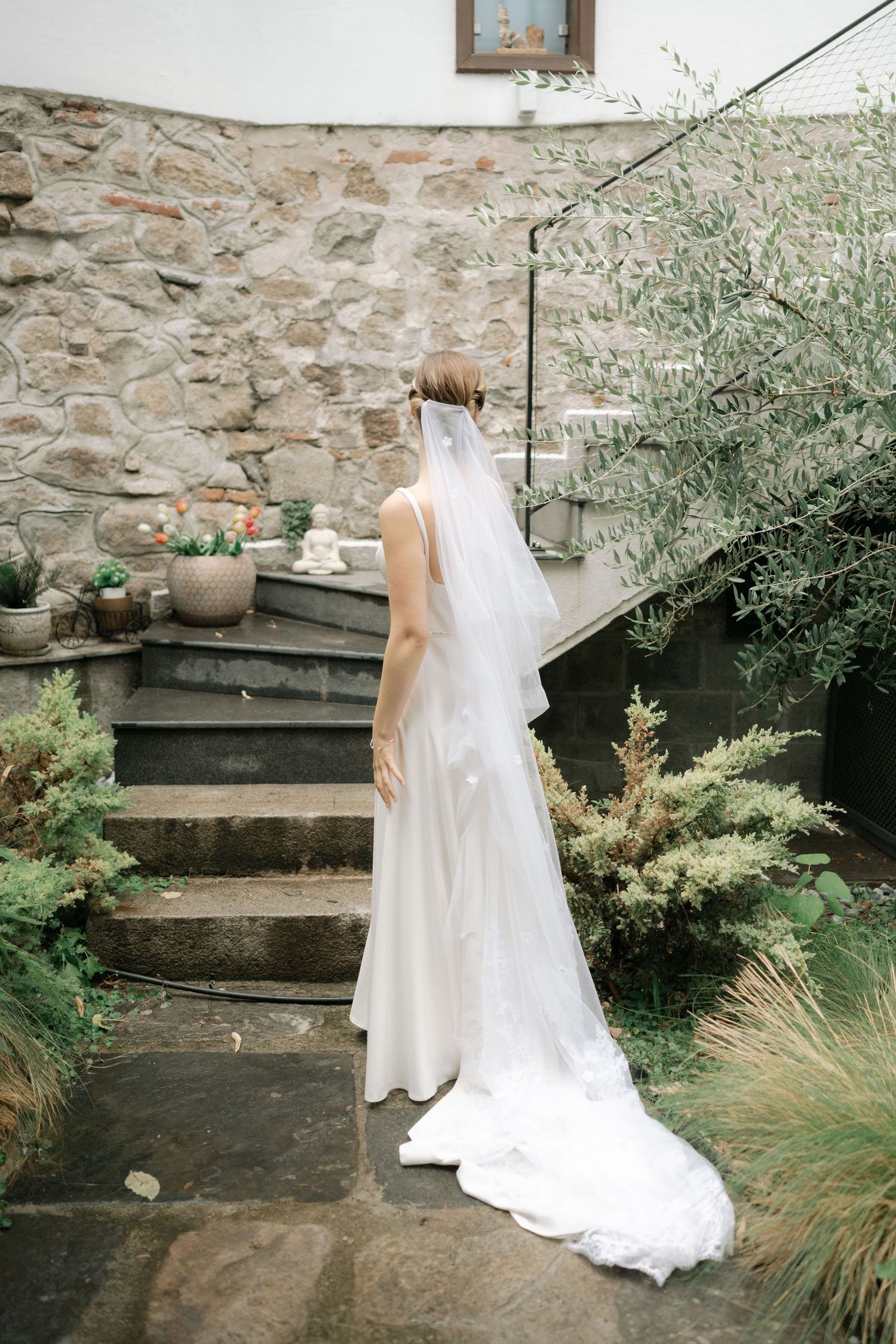 A series of elegant bridal photos showing the back of a white wedding dress against a rustic stone wall with greenery.