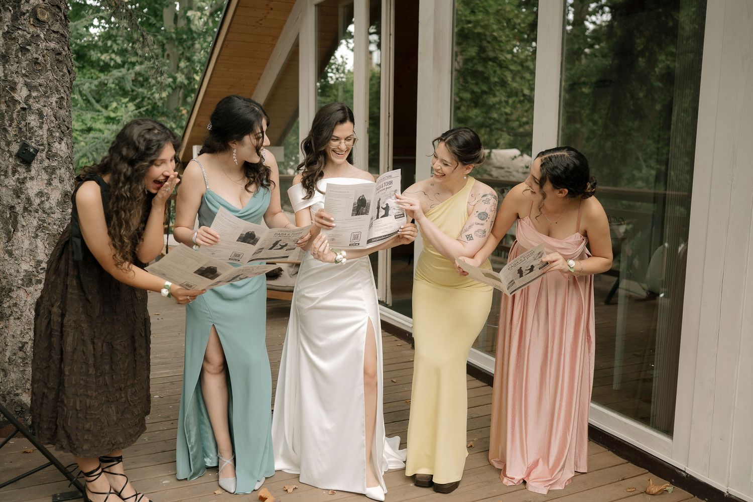 A wedding party group wearing pastel pink and blue dresses stands together in an outdoor garden setting.