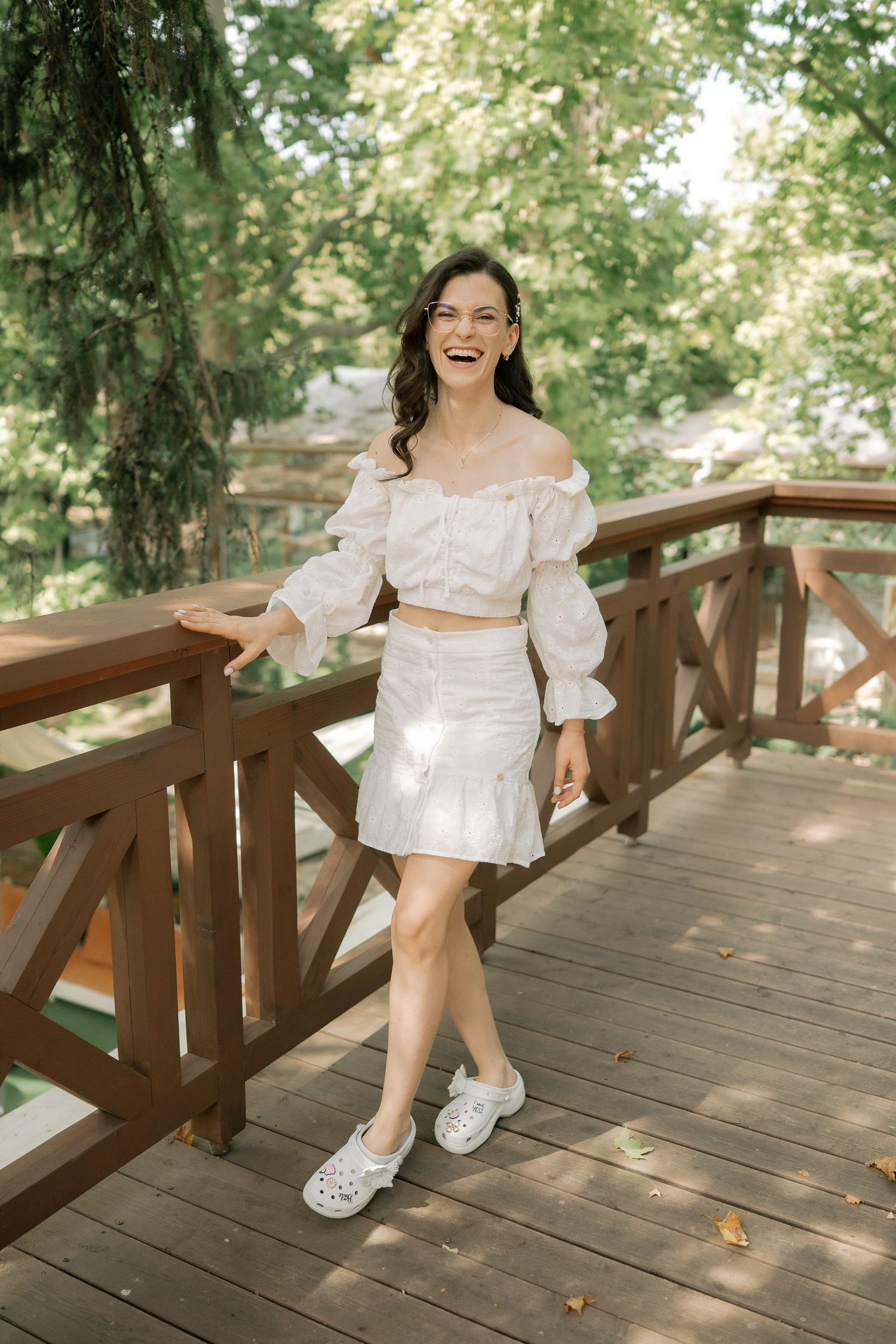 A series of photos on a wooden deck in dappled sunlight shows someone in a white summer dress and white shoes.