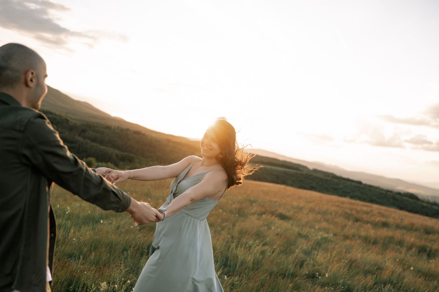 Couple dancing at sunset in a golden meadow, woman in blue dress with hair blowing in the wind.