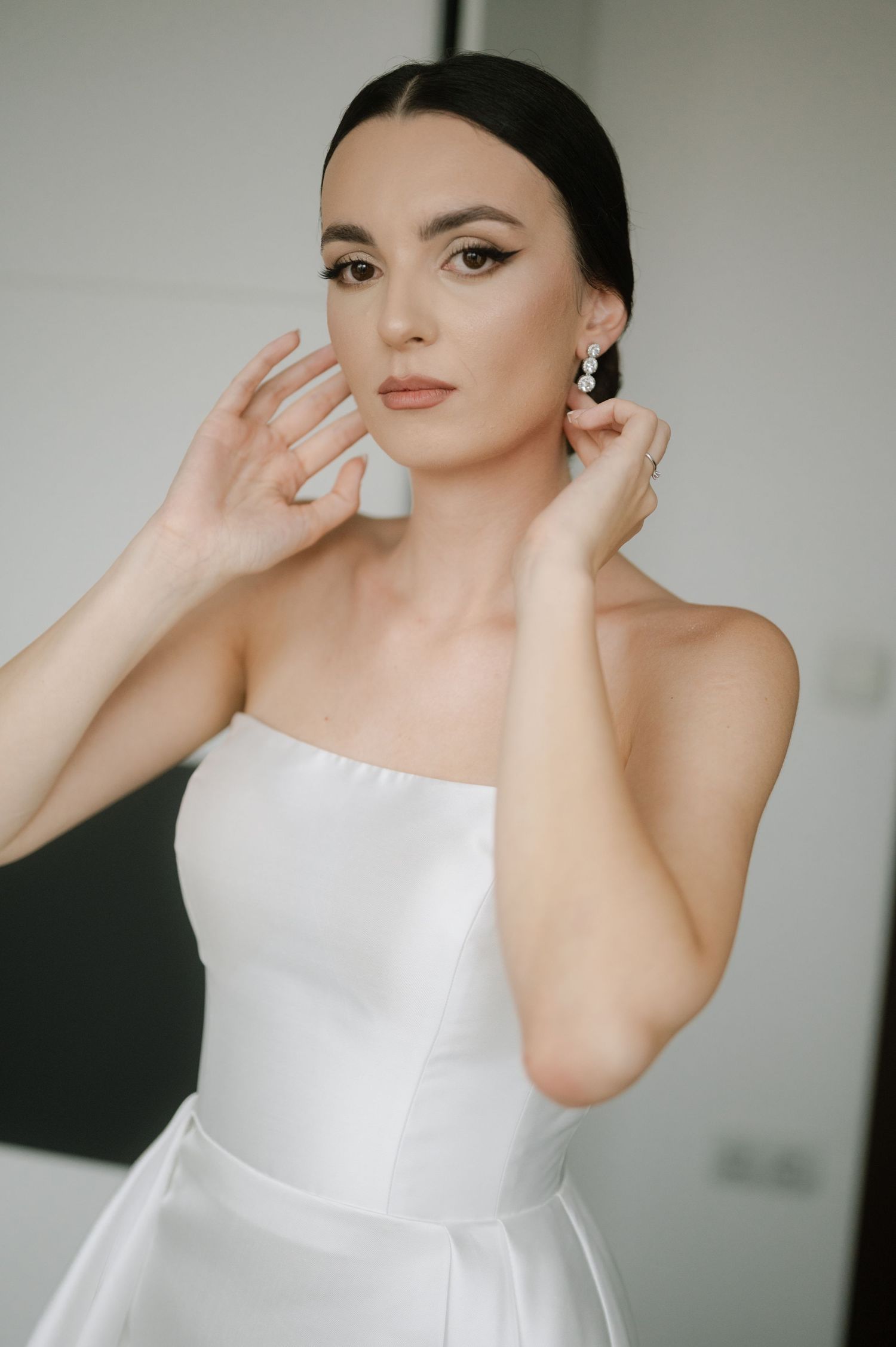 Elegant bridal portrait featuring a classic white strapless dress, pearl earrings and sophisticated makeup.