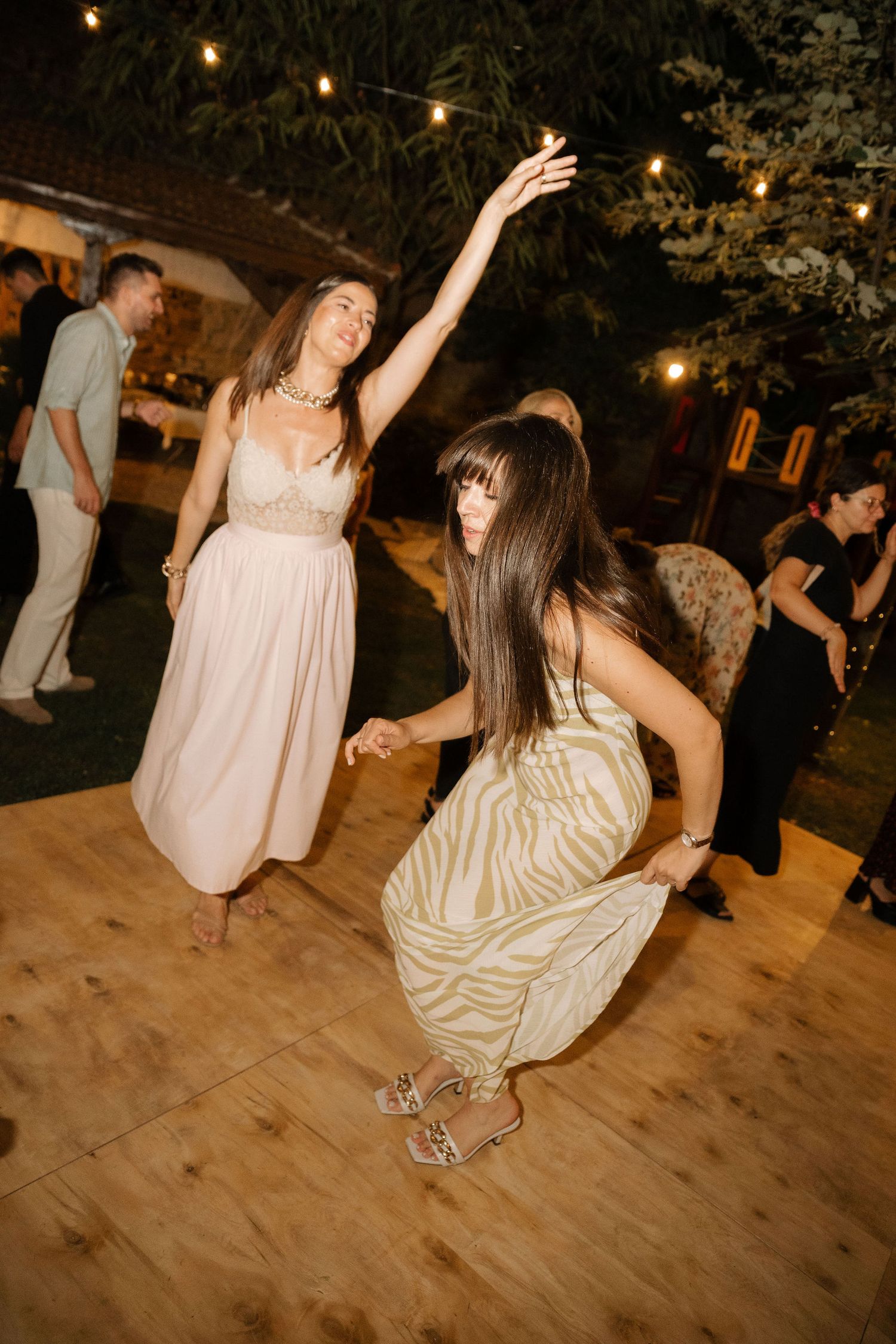 People dancing and having fun on a wooden dance floor at a party under string lights.