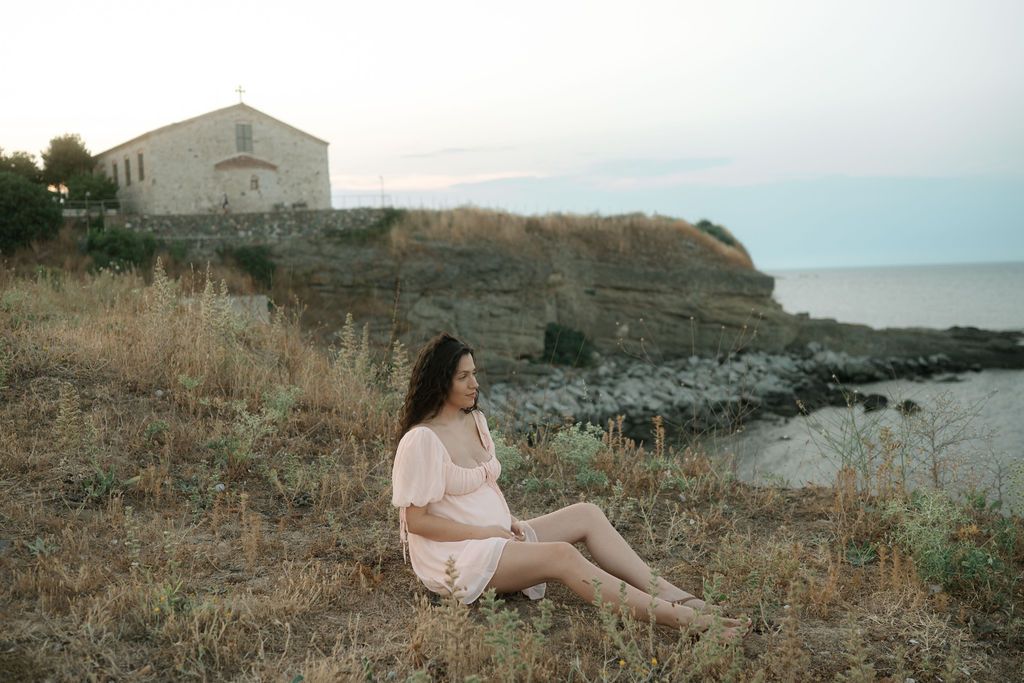 Person relaxes on rocky coastal cliffs overlooking the ocean at sunset.