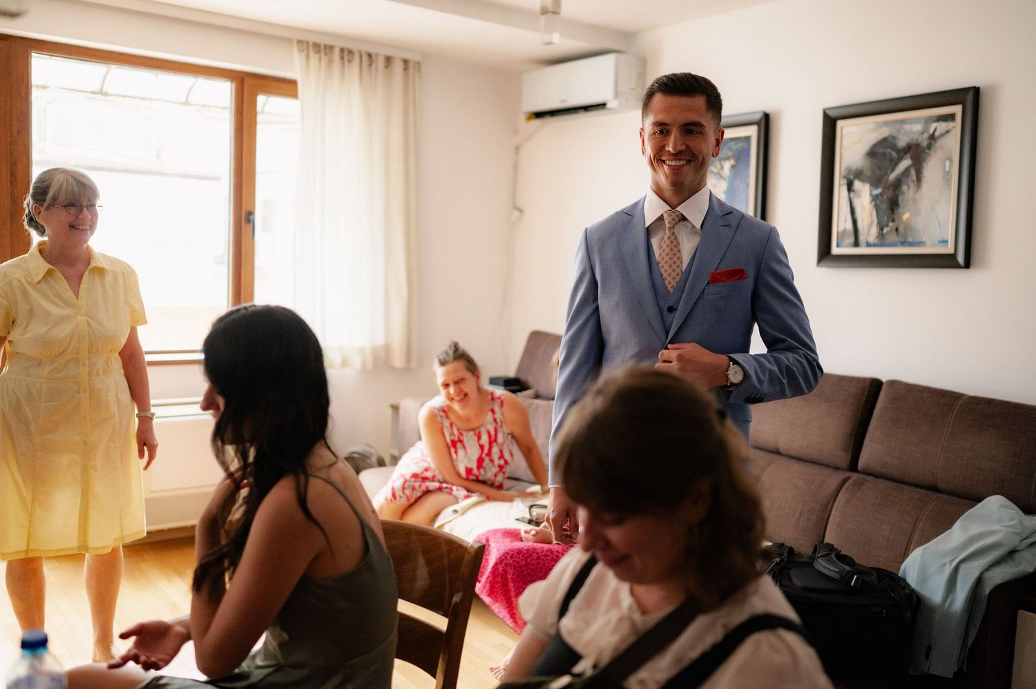 People gathered in a bright room with framed artwork on the wall during what appears to be a social event.