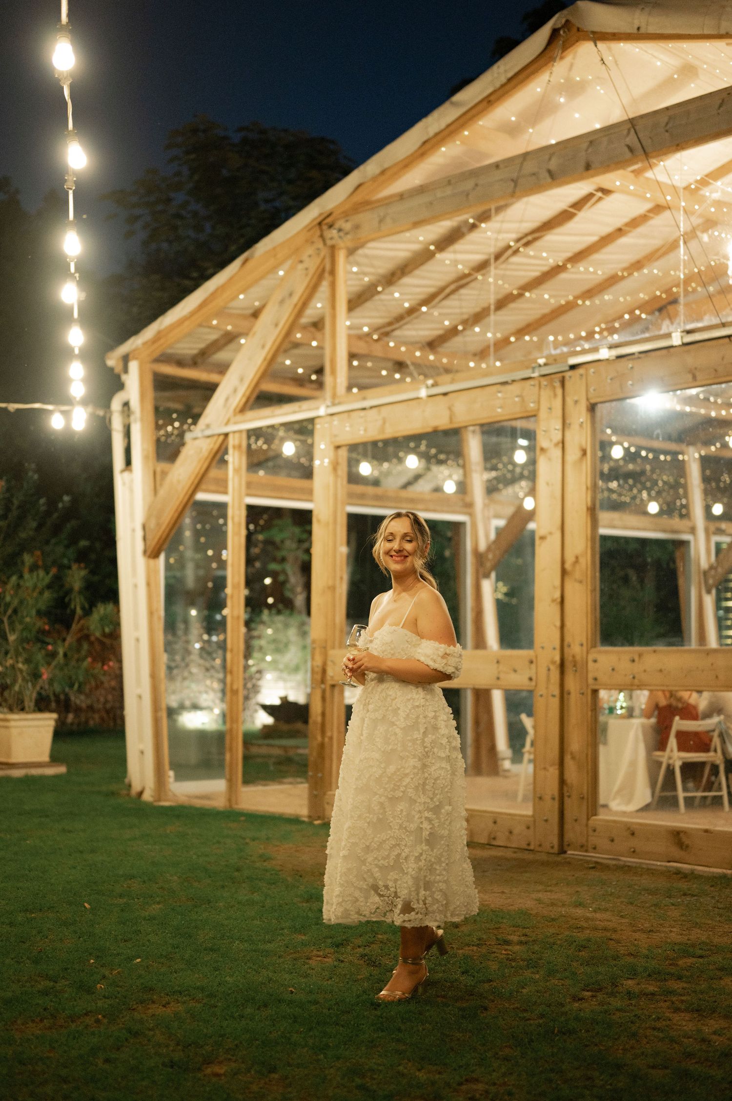 A rustic wooden pavilion with string lights illuminates a romantic wedding scene at dusk in an outdoor garden setting.