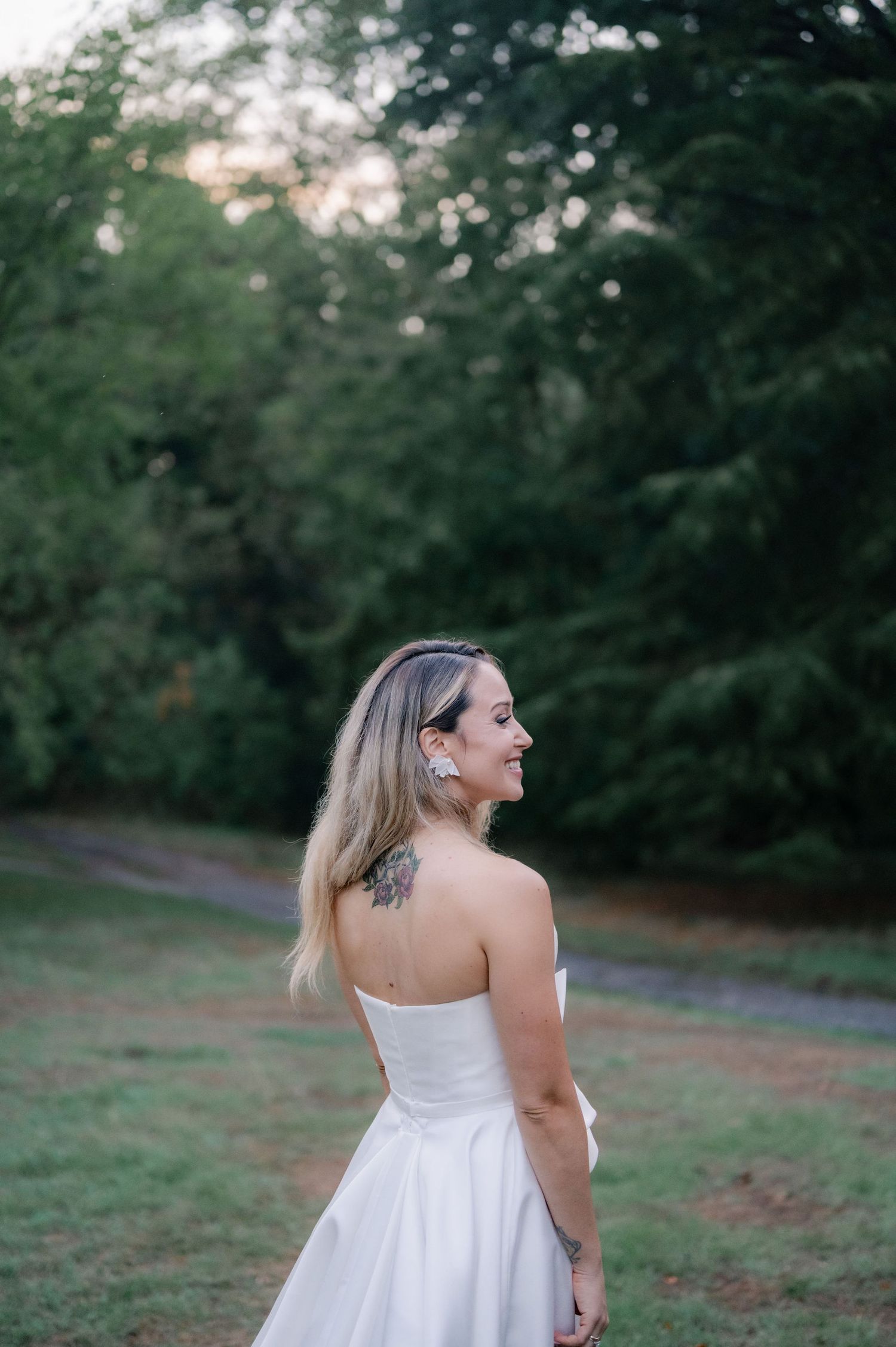 Woman in white dress twirls joyfully in a lush green outdoor setting during golden hour.