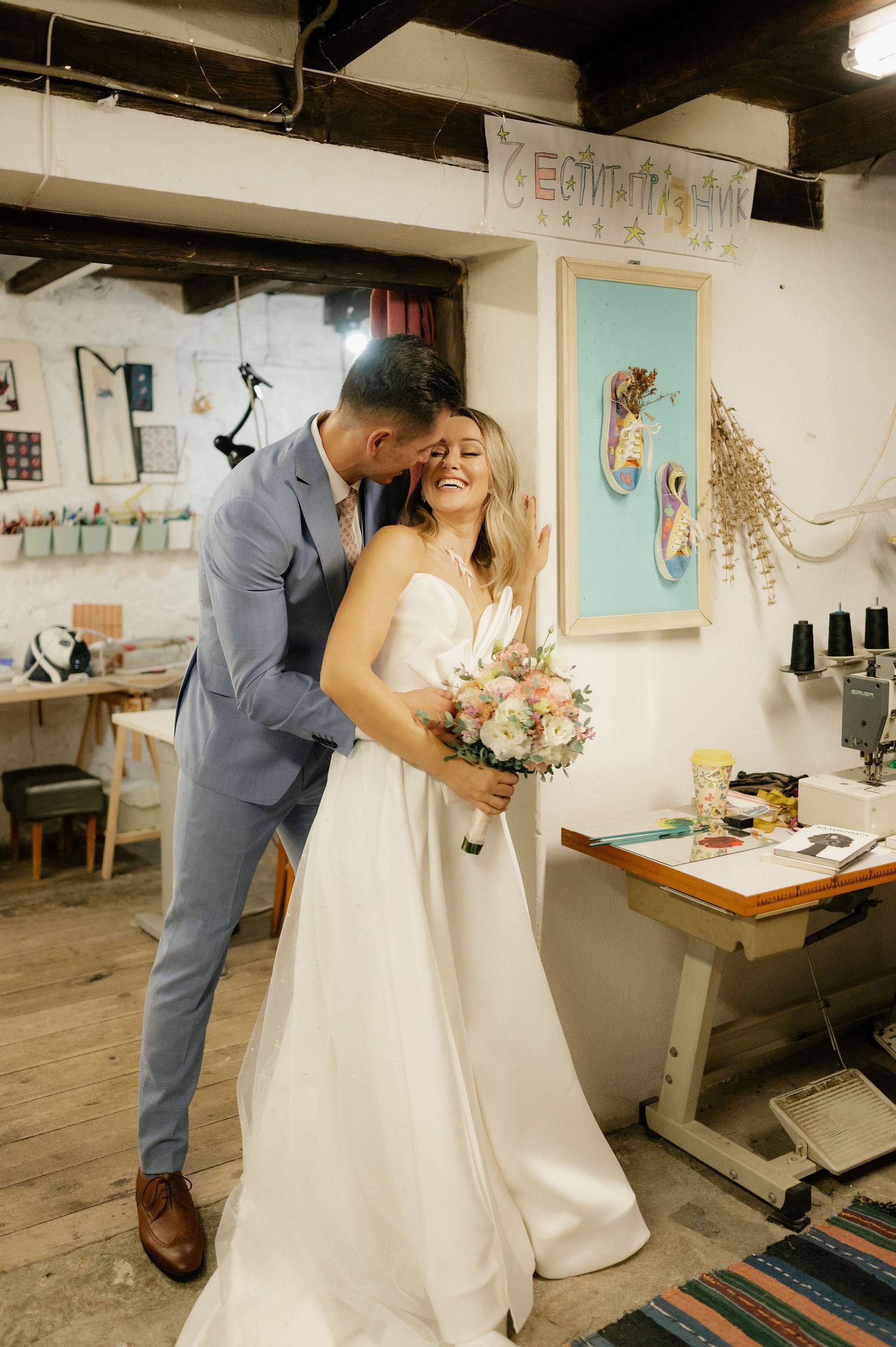 A couple shares a joyful moment in their wedding attire inside an artistic studio space with a turquoise door and decor.