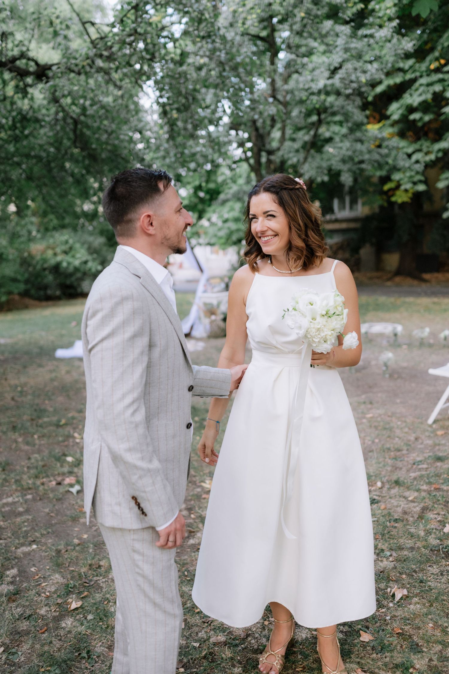 A couple in white attire shares joyful moments during an outdoor photo session in a garden setting.