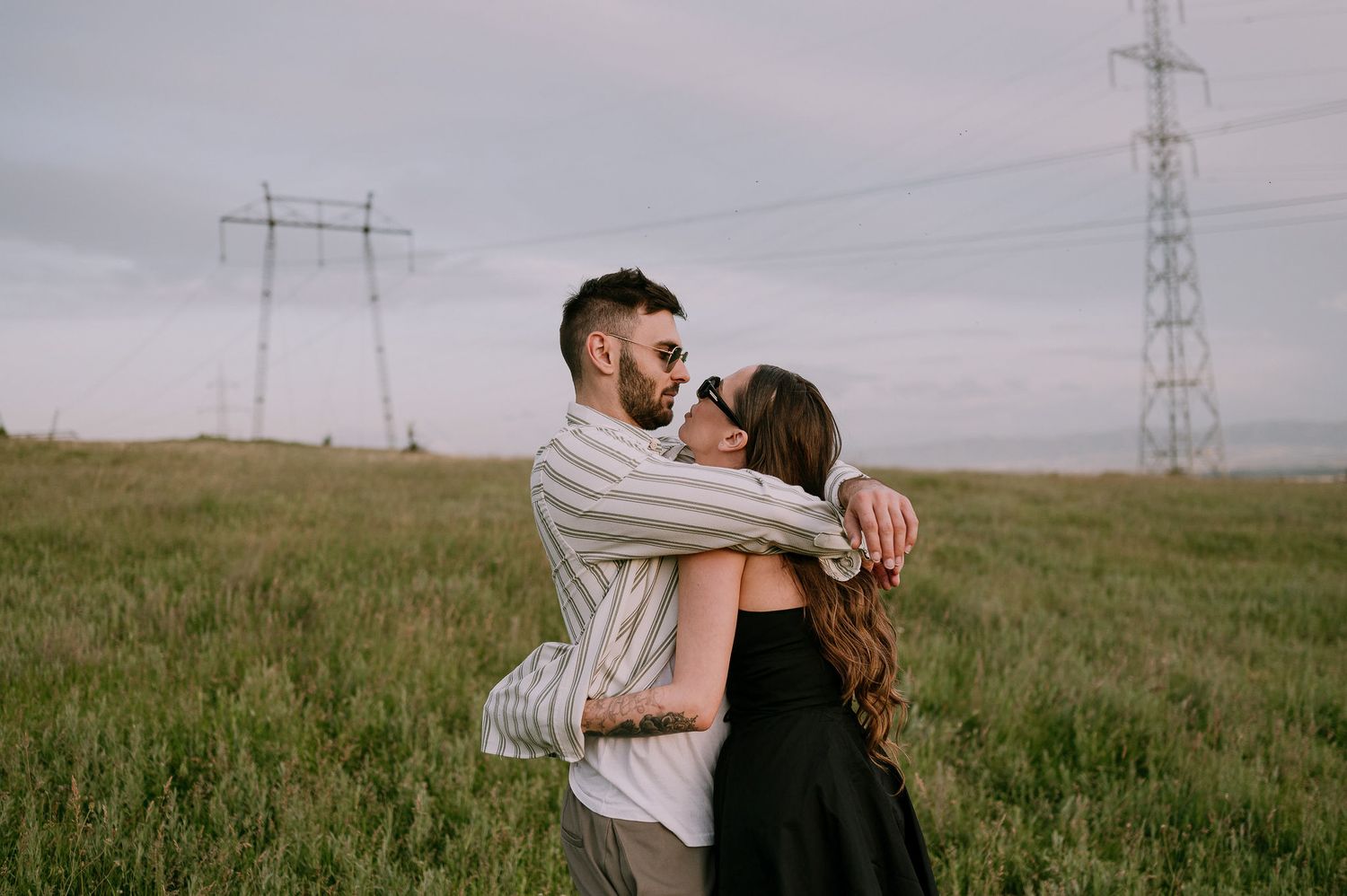 Couple embraces in a romantic moment against a backdrop of power lines and rolling green hills.