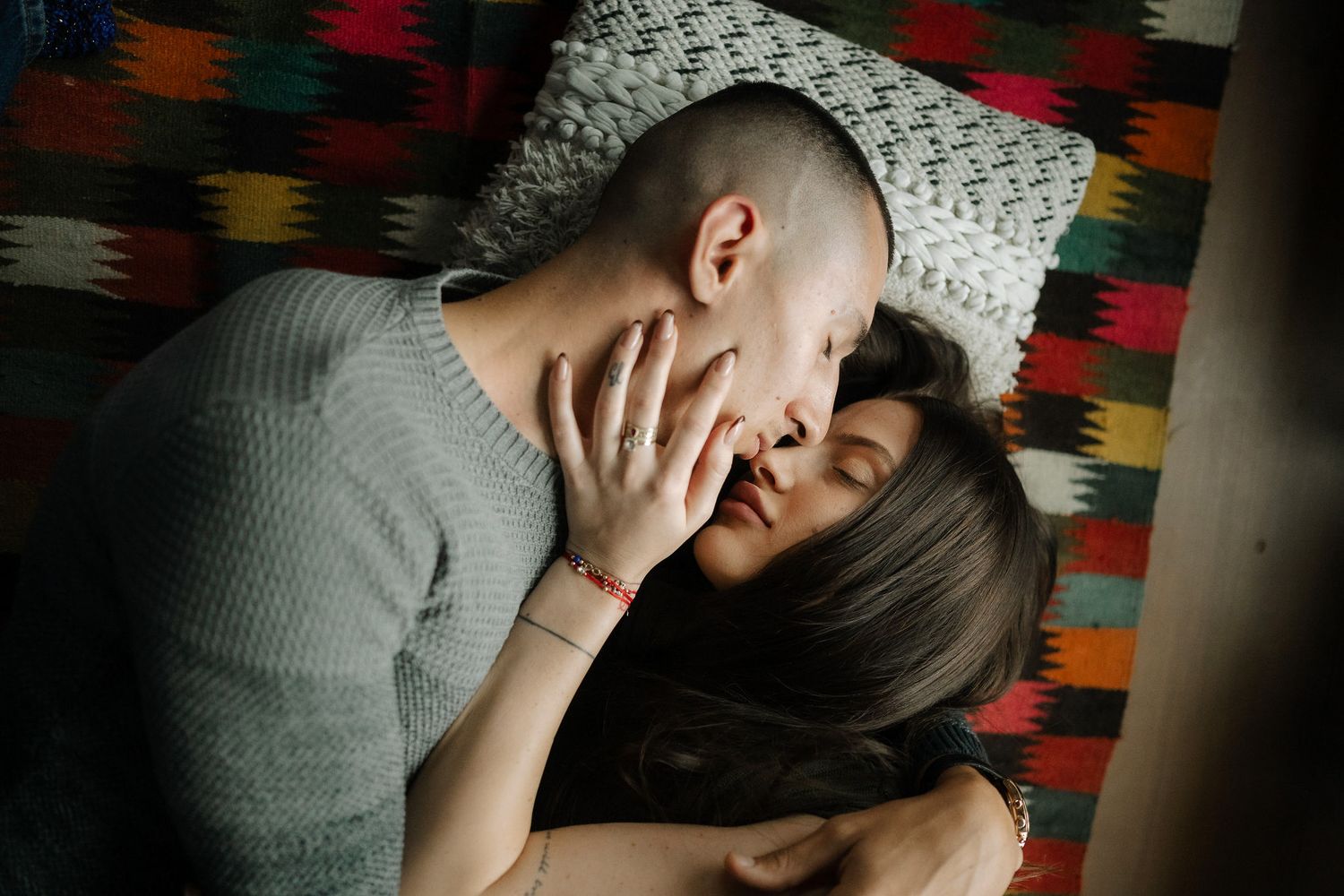 Person in gray sweater sitting against colorful patterned wall appears distressed with hand covering face.