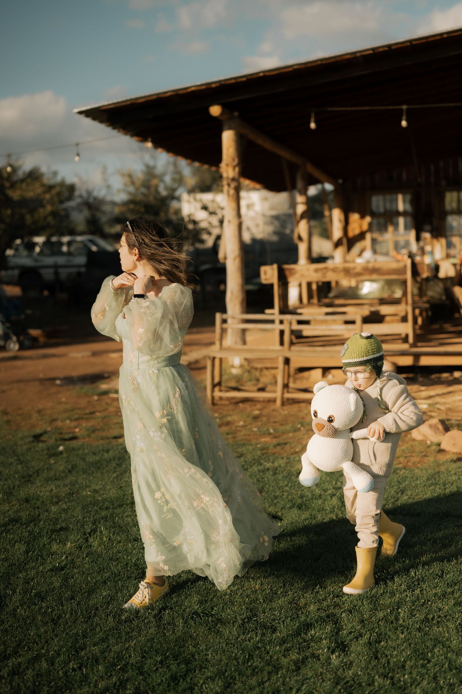 A whimsical scene with a flowing white dress and a small figure in a puffy astronaut costume on grassy ground at sunset.