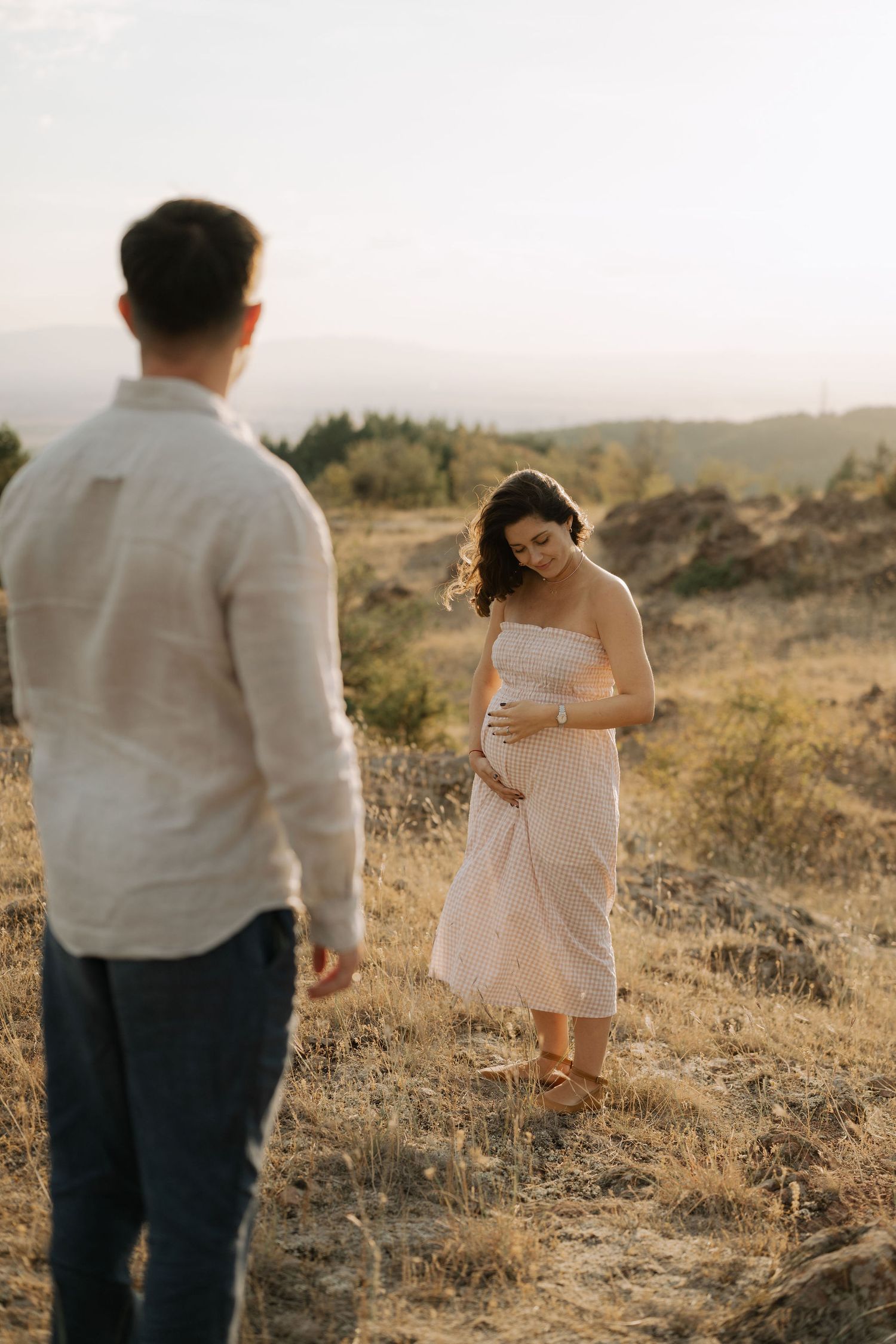 Couple in white and dark attire poses romantically in a golden field during sunset for engagement photos.