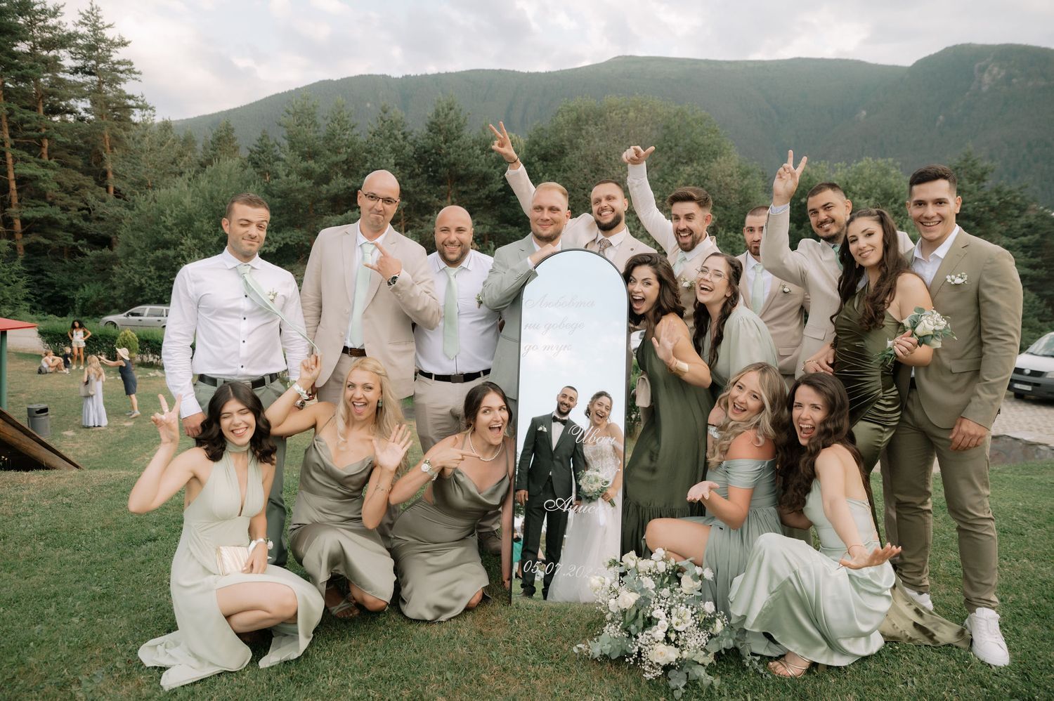 Wedding party poses together on grassy hillside wearing coordinated gray and white attire for outdoor celebration.