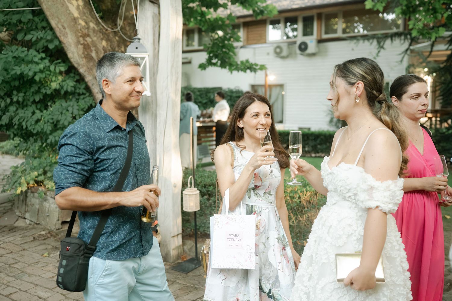 A group of people enjoying a casual outdoor gathering with drinks and conversation in a garden setting.