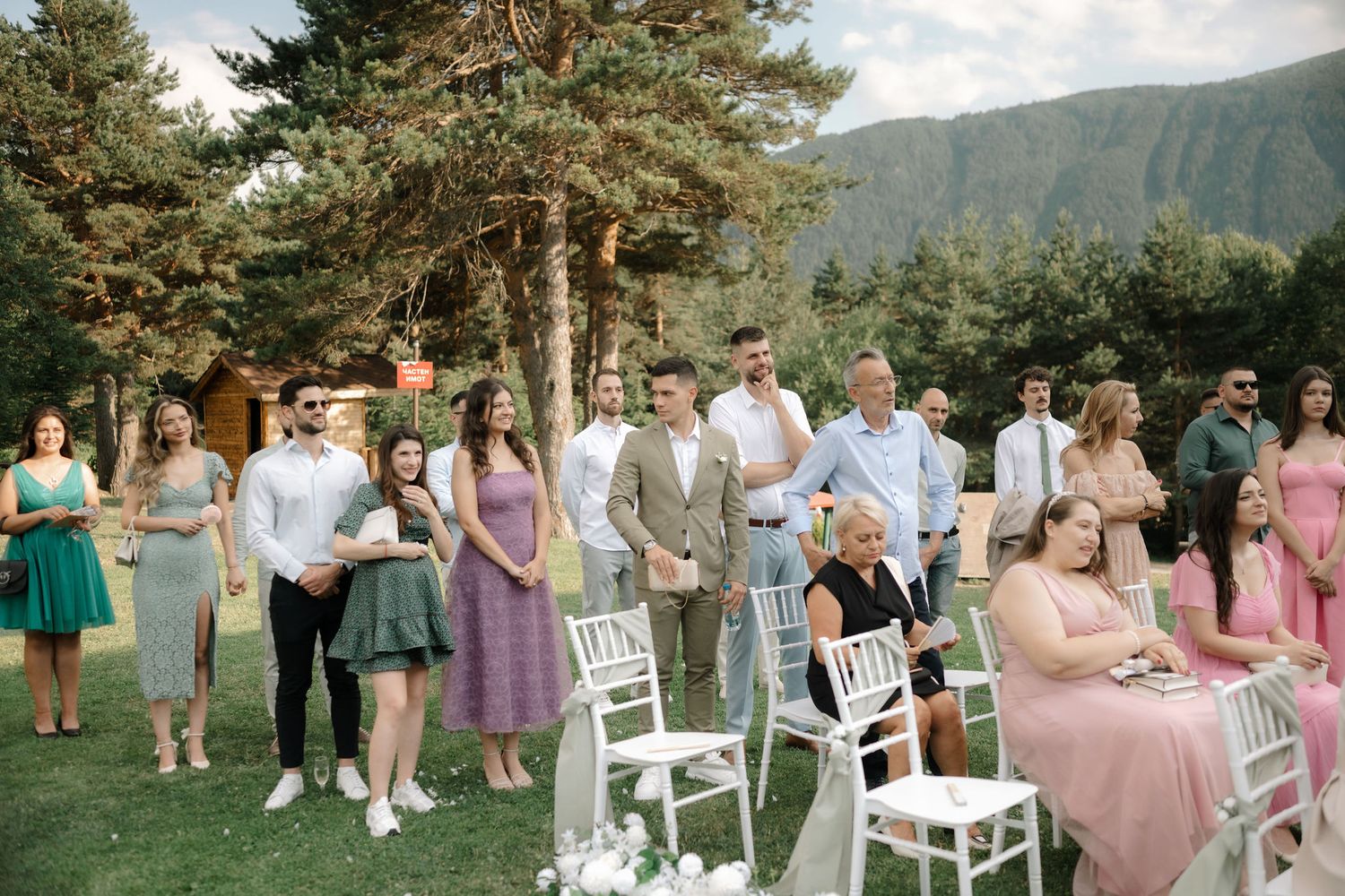 Wedding party gathers outdoors for group photos in a scenic mountain setting with pink bridesmaid dresses.